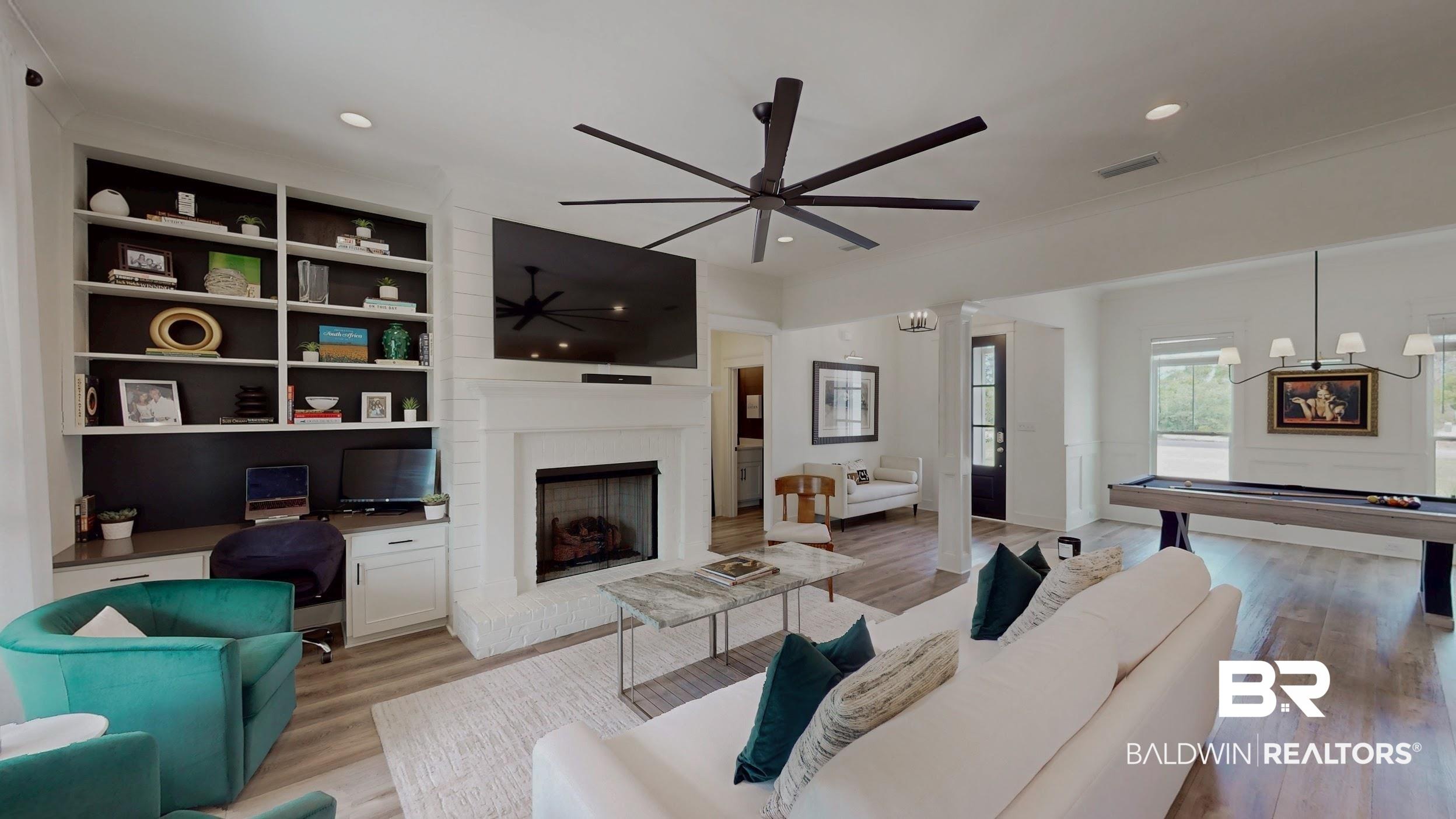 Image 2: Spacious living area featuring light wood-finish flooring, a white brick fireplace with mantel, and built-in shelving with integrated desk space