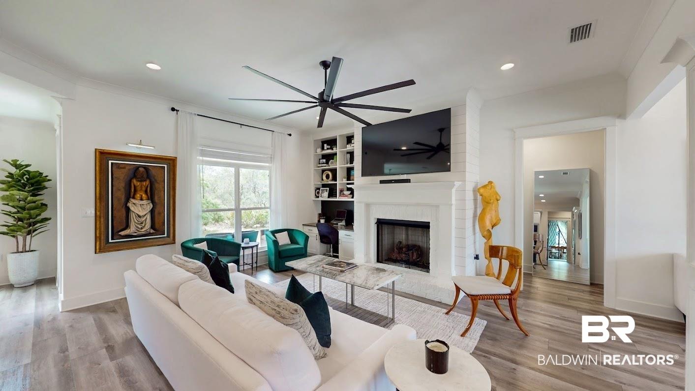 Image 3: Living area featuring wood-finish flooring, a white brick fireplace with mantel, built-in shelving, a large window, and recessed lighting