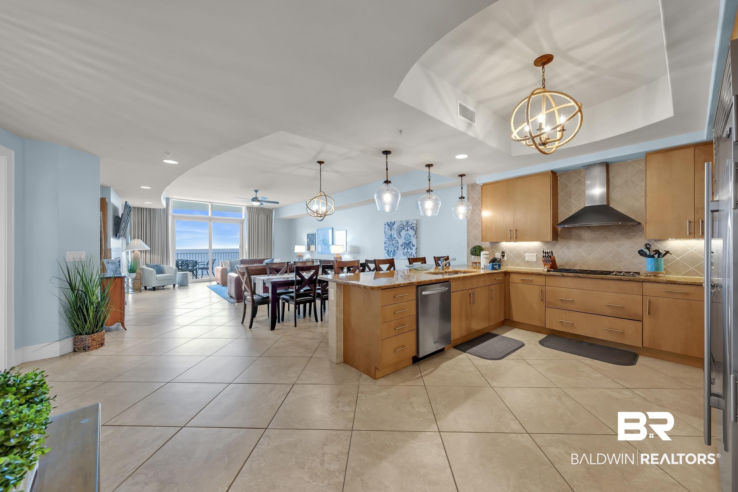 Image 3: Open-concept living space featuring a full kitchen with light wood cabinetry, a tile backsplash, and a stainless steel range hood