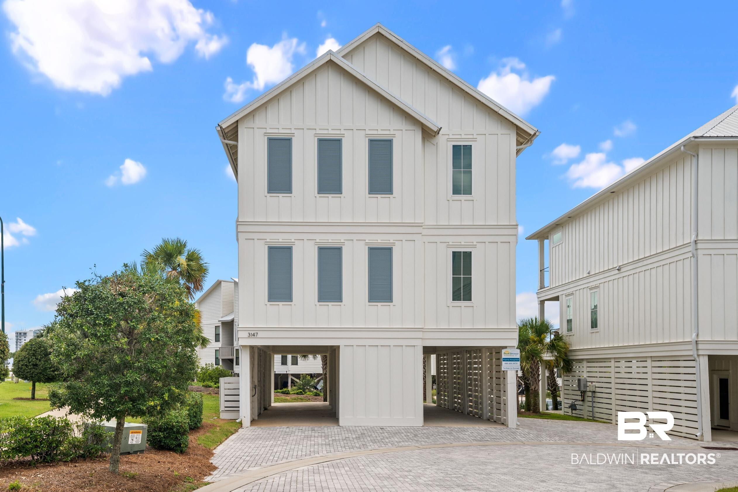 Image 1: Coastal inspired home with board and batten siding, a carport, and decorative driveway