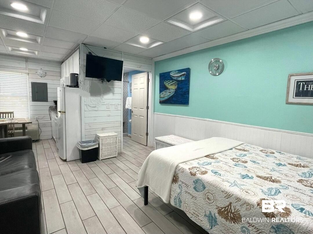 Image 2: Bedroom featuring wood walls, wood finish floors, freestanding refrigerator, a wainscoted wall, and a paneled ceiling