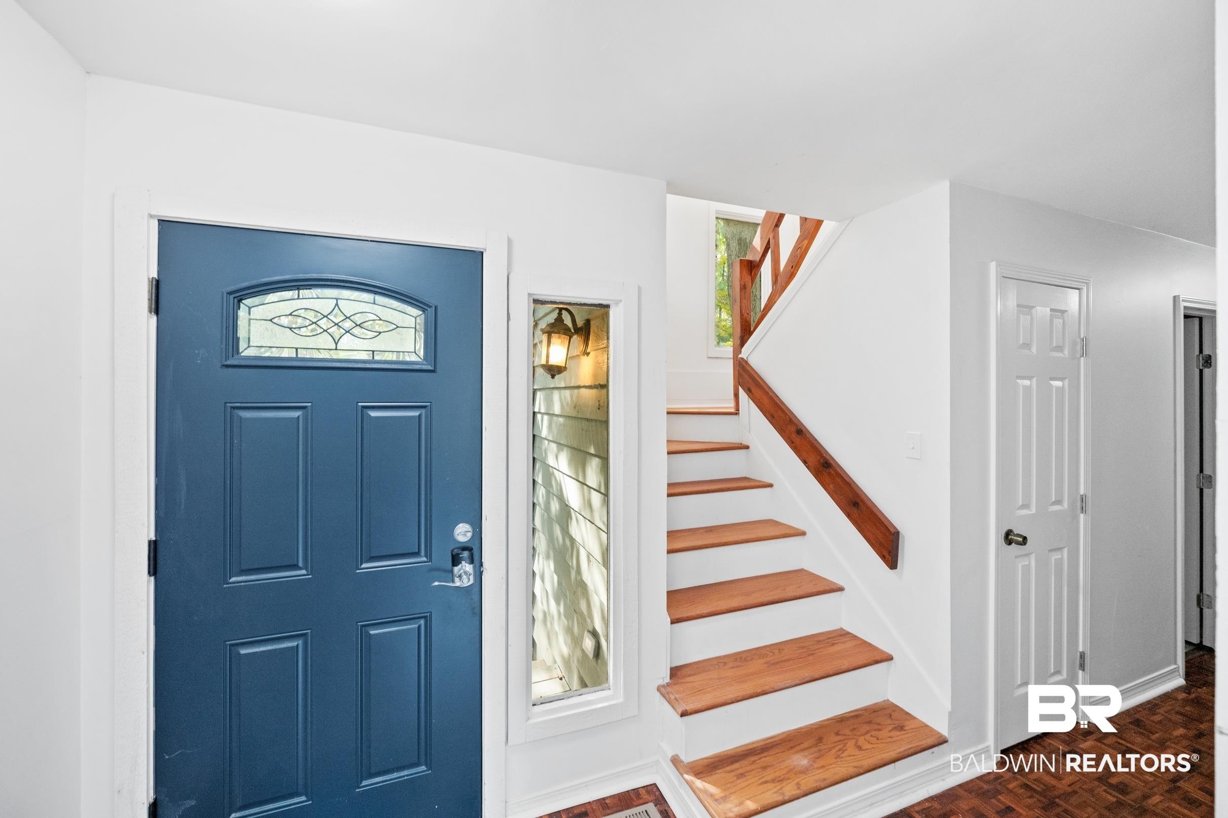 Image 4: Entryway featuring a paneled blue door with decorative glass, a sidelight, wood-finish flooring, a staircase with wood treads and railing, and white walls
