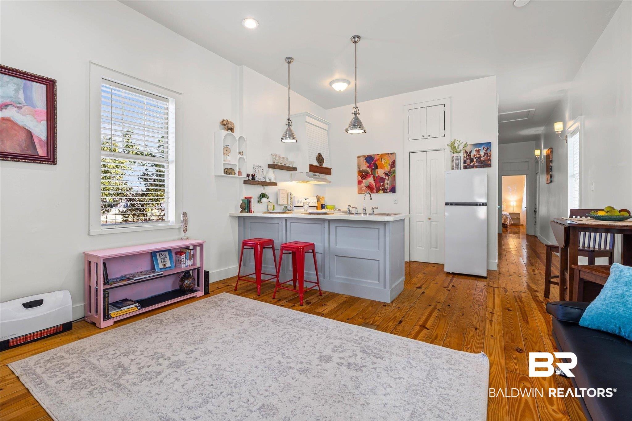 Image 4: Open-concept living space featuring wood-finish flooring, recessed lighting, a kitchen island with seating, and a large window providing natural light