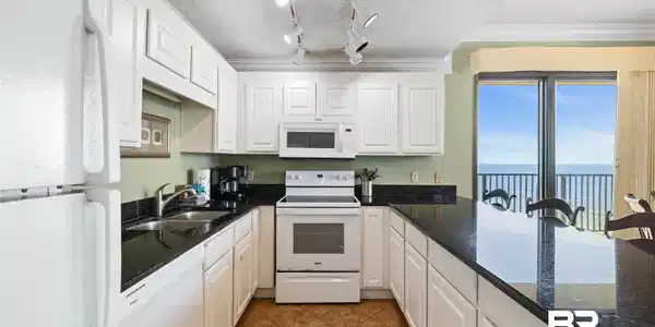 Image 3: Kitchen featuring white cabinetry, black stone countertops, track lighting, and stainless steel sink
