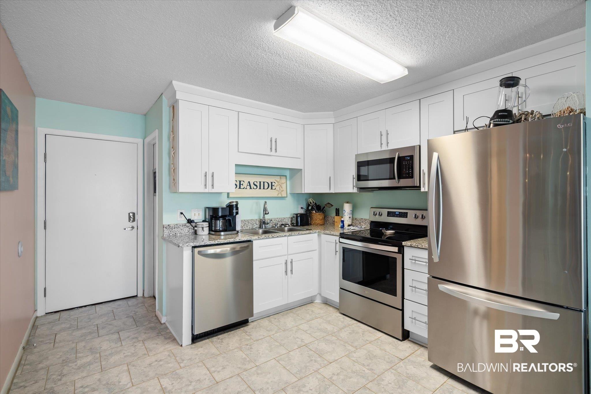 Image 2: Kitchen with sink, light stone countertops, white cabinets, appliances with stainless steel finishes, and a textured ceiling