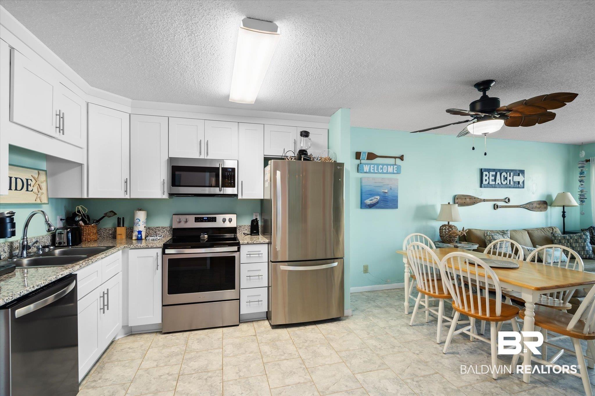 Image 4: Kitchen with light stone countertops, appliances with stainless steel finishes, sink, a textured ceiling, and white cabinetry