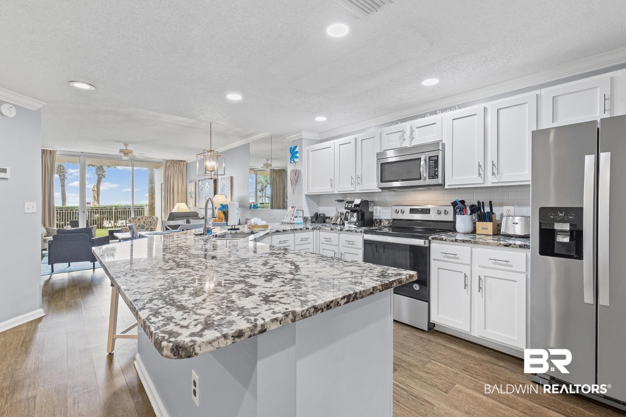 Image 2: Kitchen featuring appliances with stainless steel finishes, a peninsula, light stone countertops, white cabinets, and crown molding