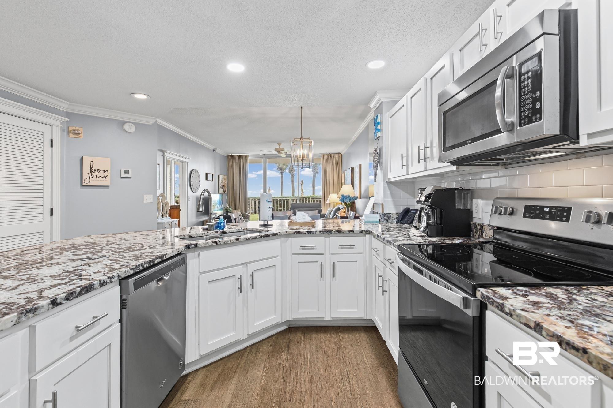 Image 3: Kitchen with appliances with stainless steel finishes, white cabinets, light stone countertops, ornamental molding, and dark wood-type flooring
