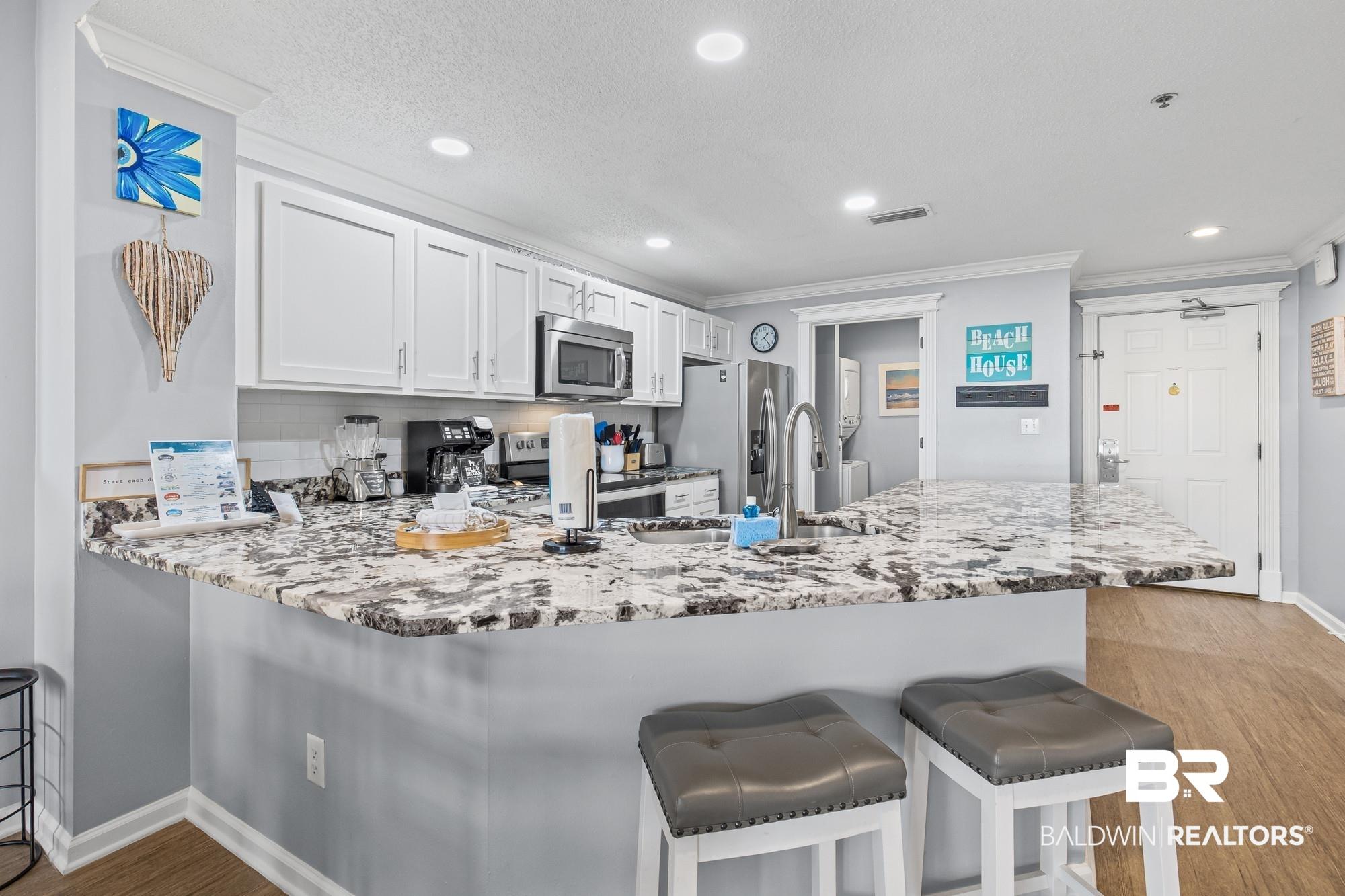 Image 4: Kitchen with a breakfast bar, a peninsula, white cabinets, light wood-style flooring, and light stone countertops