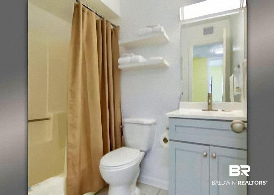Image 4: Bathroom featuring a light-colored shower surround, a toilet, a vanity with a light blue cabinet, a white countertop, and a wall-mounted mirror