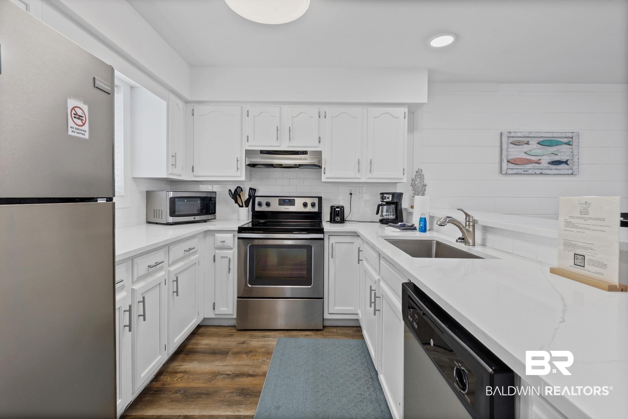 Image 4: Kitchen featuring stainless steel appliances, white cabinets, dark wood-type flooring, light stone counters, and backsplash