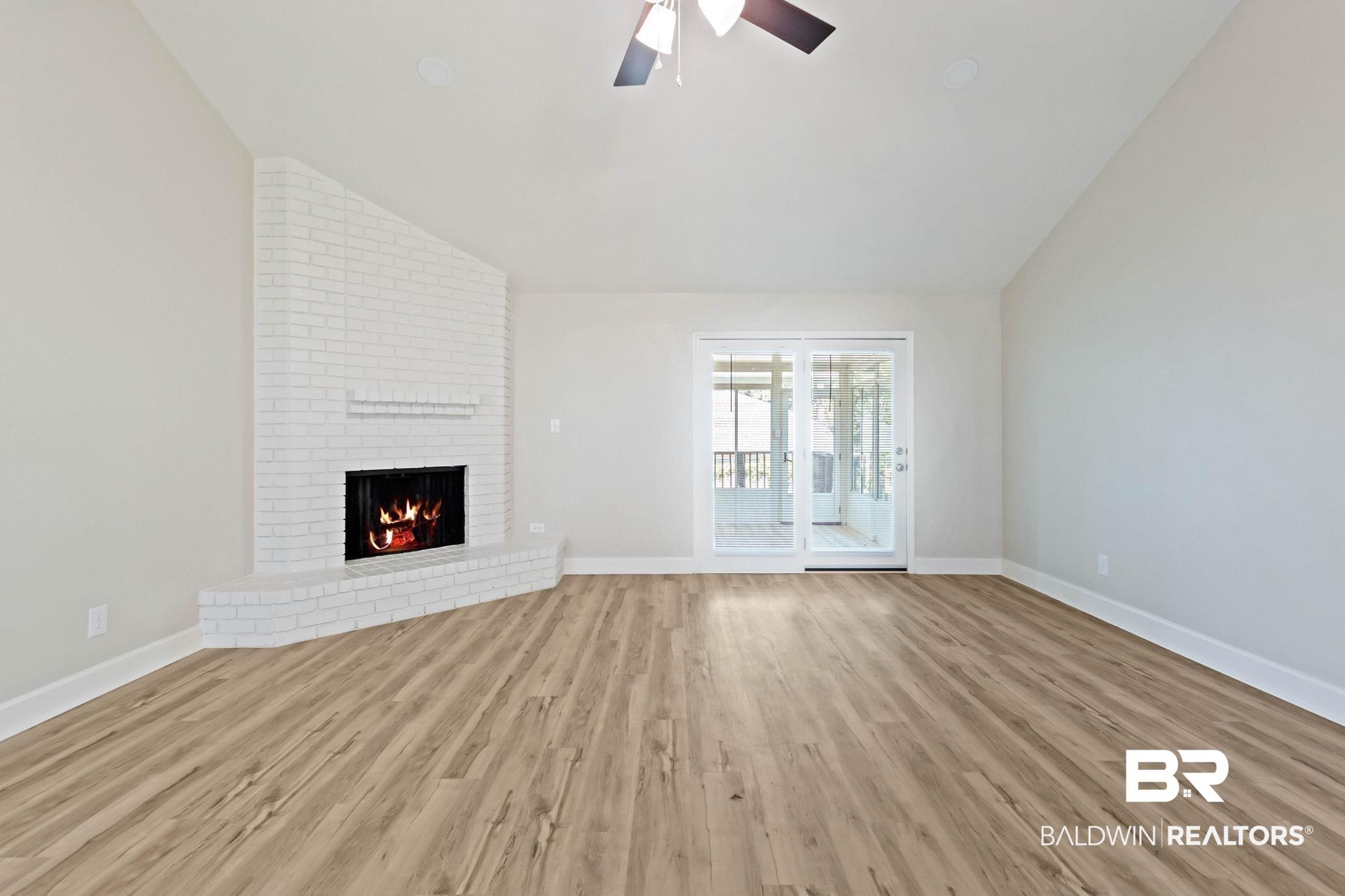 Image 3: Spacious interior featuring wood-finish flooring, a white brick fireplace with hearth, vaulted ceilings, and a ceiling fan