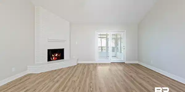 Image 3: Spacious interior featuring wood-finish flooring, a white brick fireplace with hearth, vaulted ceilings, and a ceiling fan