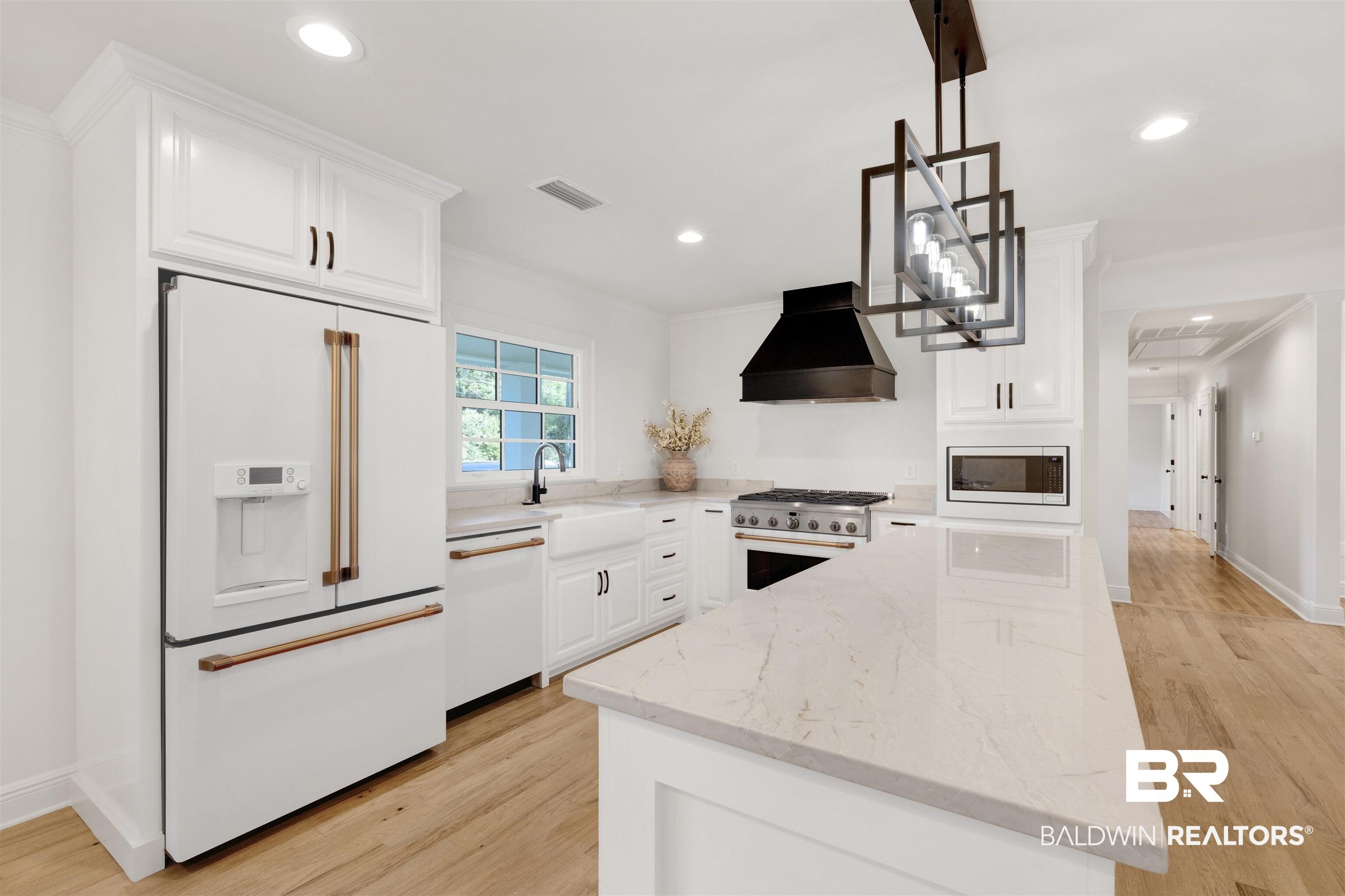 Image 4: Kitchen featuring light wood finished floors, high end appliances, white cabinetry, light stone counters, and decorative light fixtures