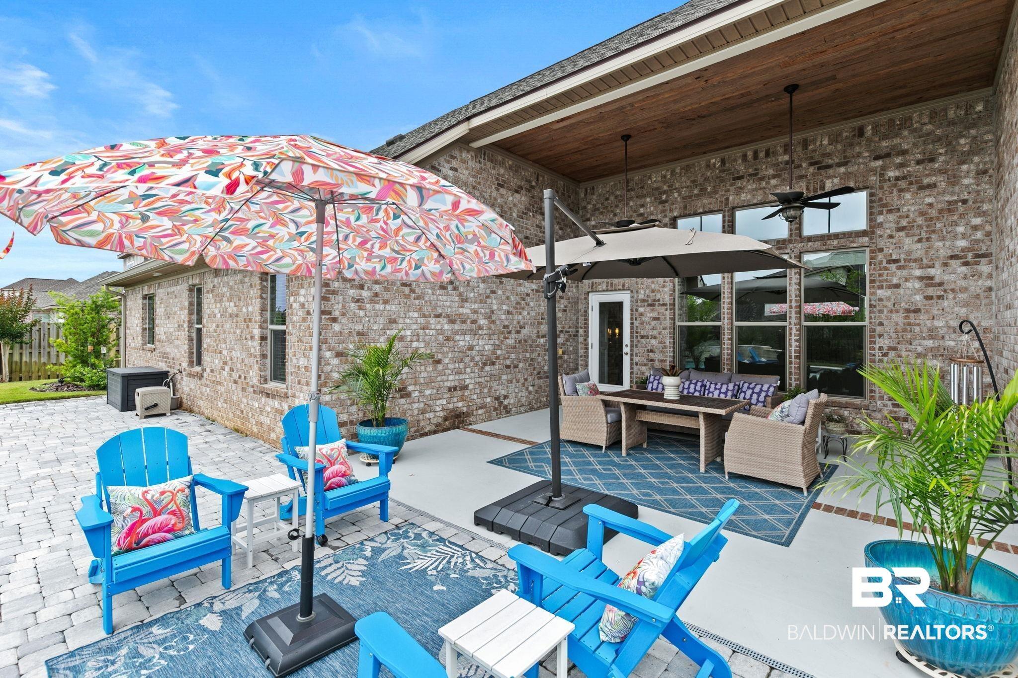 Image 3: Expansive outdoor living area featuring a covered patio with wood-finish ceiling and ceiling fans, large windows, and a brick exterior