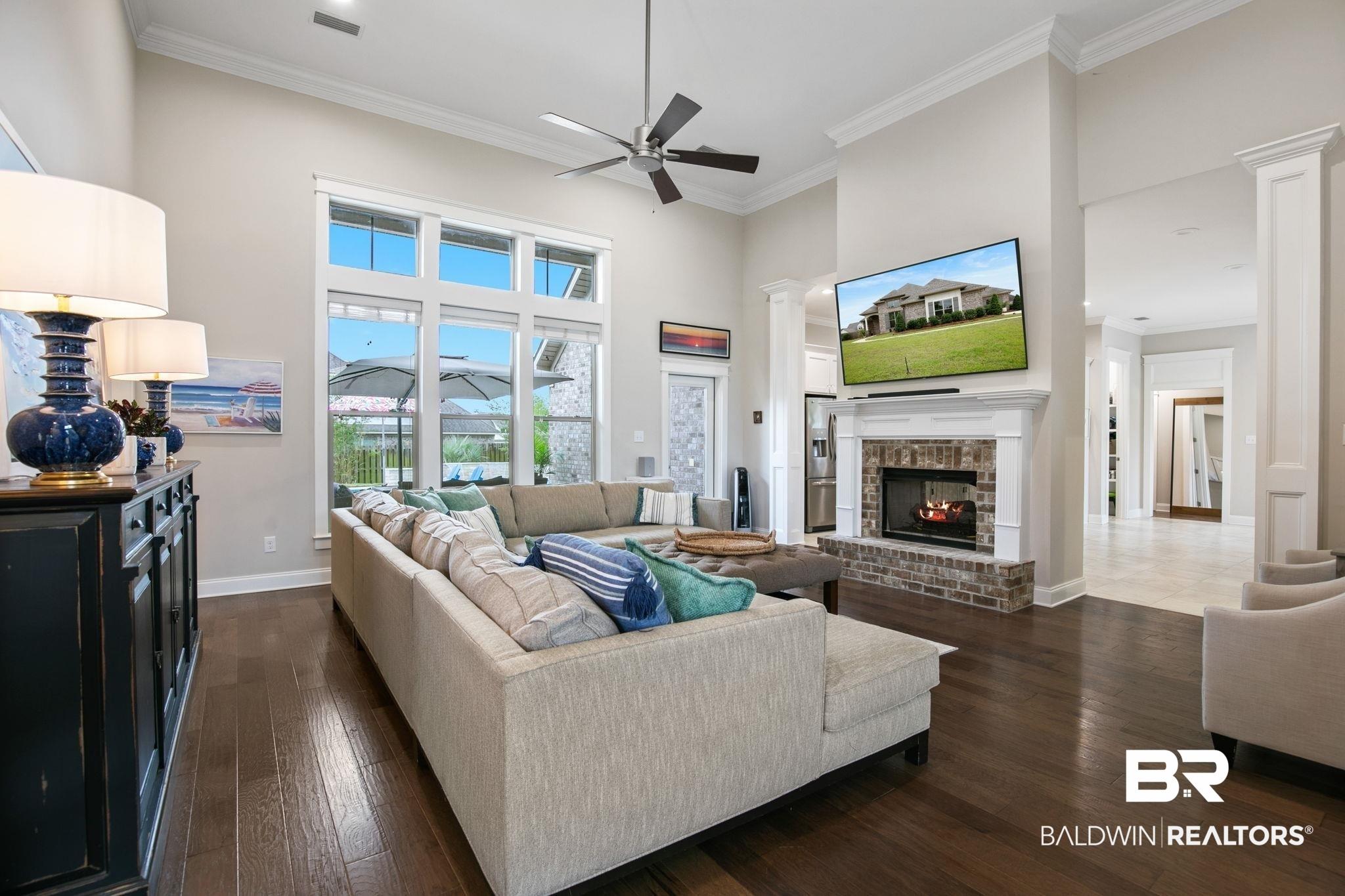 Image 4: Spacious living area featuring high ceilings, dark wood-finish flooring, and a fireplace with a brick surround and white mantel