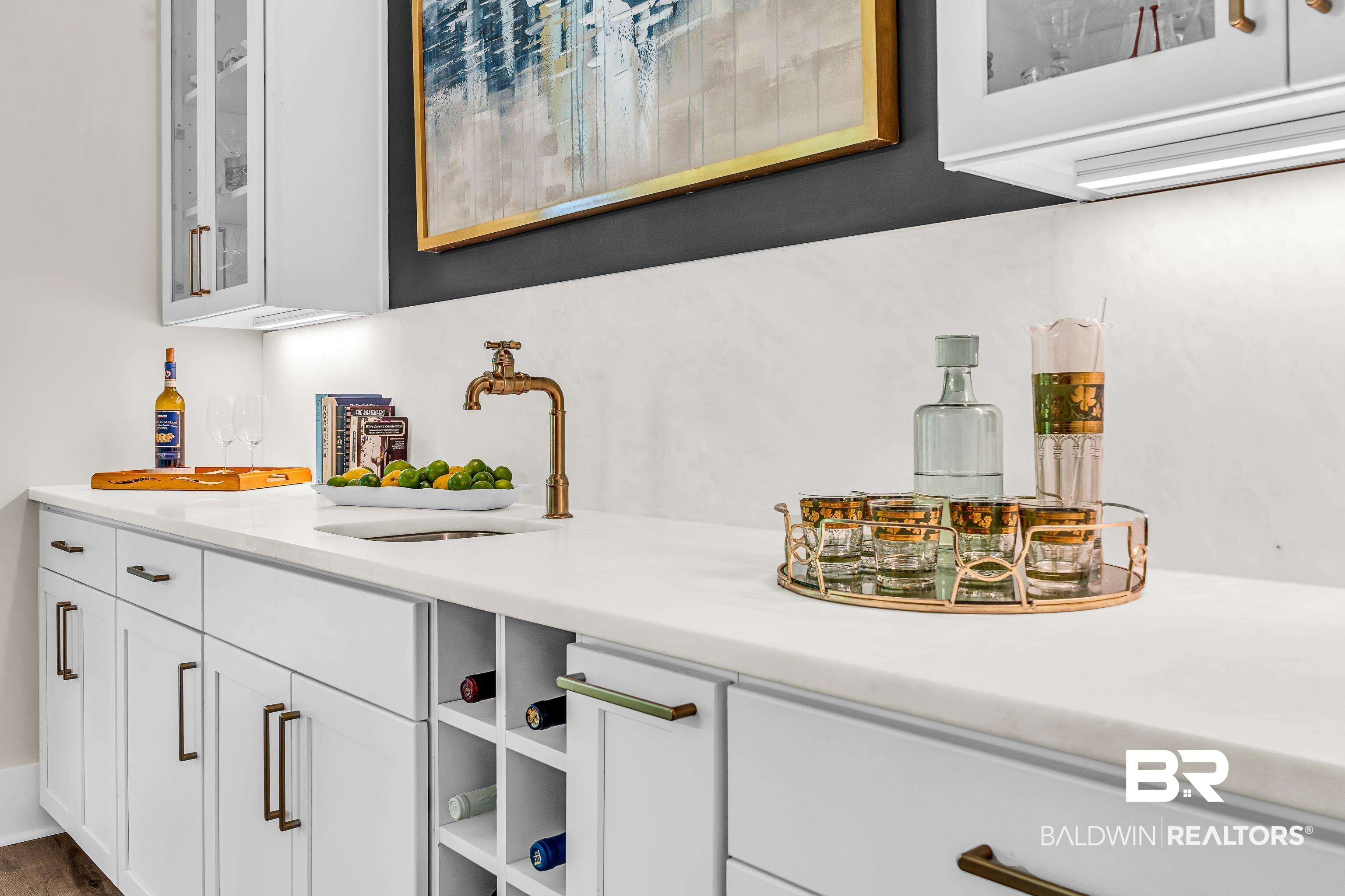 Image 2: Built-in wet bar featuring white cabinetry, a light-toned countertop, and an integrated sink with a brass-finish faucet