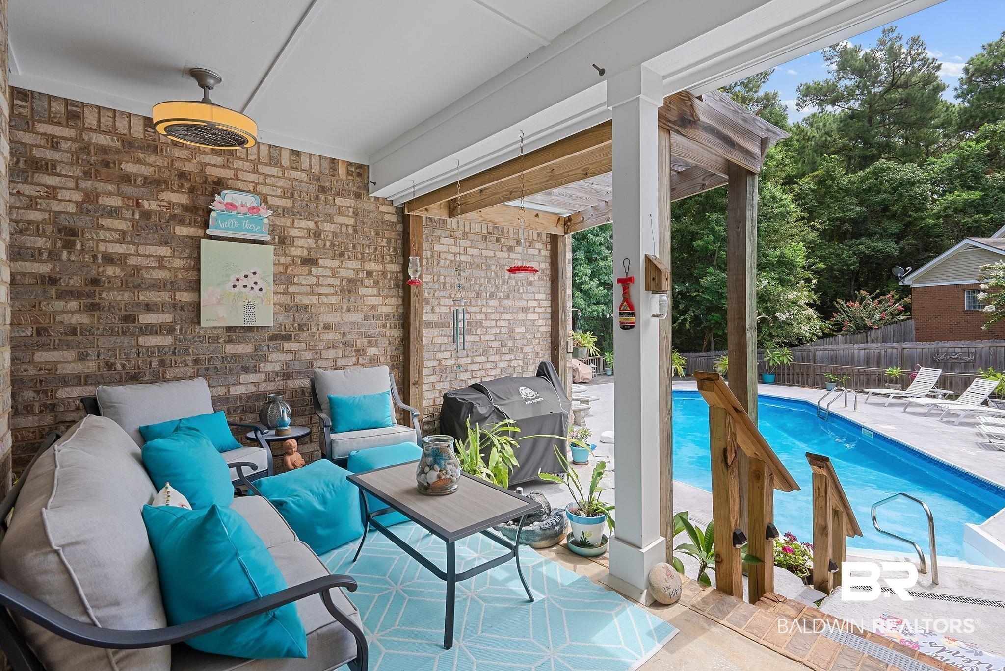 Image 3: Covered patio featuring a brick accent wall, a ceiling fan, and direct access to an in-ground swimming pool with a surrounding concrete deck