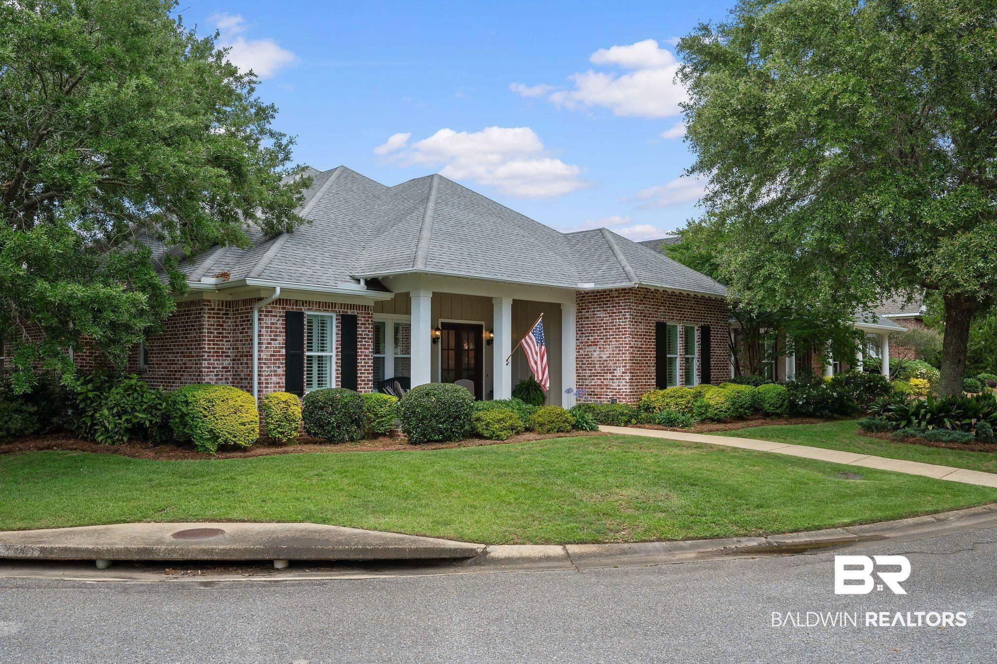 Image 2: Brick exterior residence featuring a covered front porch, dark wood double entry doors, contrasting black shutters, a gabled roofline, and established landscaping