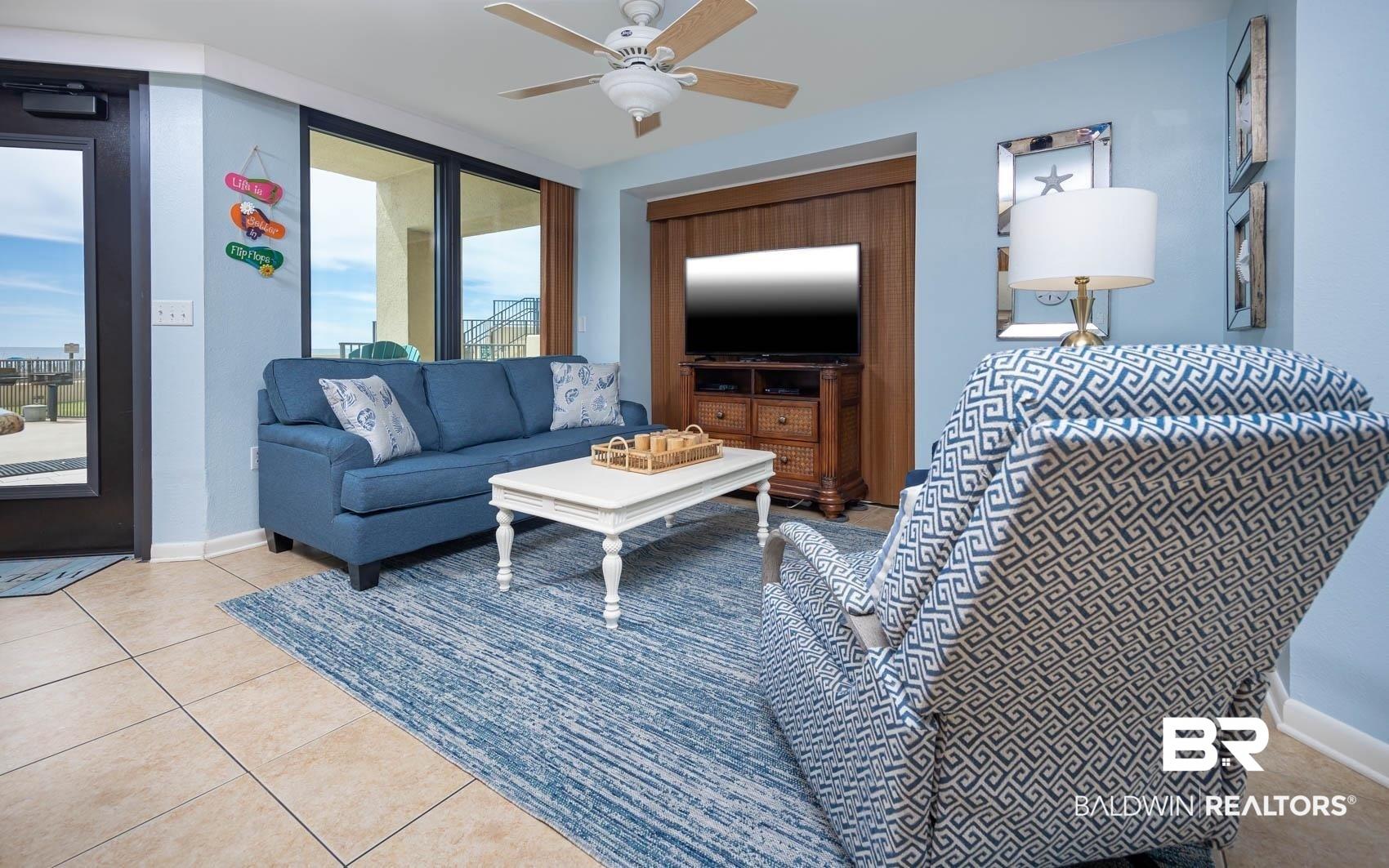 Image 2: Open-concept living space featuring neutral tile flooring, a ceiling fan, and large glass sliding doors providing outdoor access