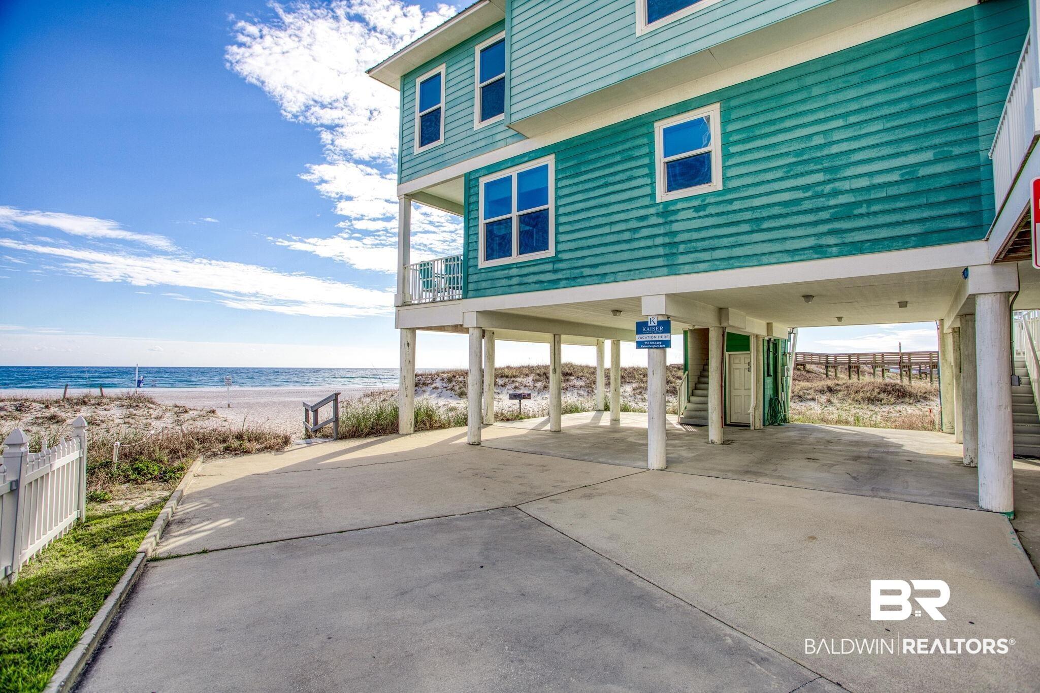 Image 3: View of patio / terrace featuring a carport, concrete driveway, stairs, a view of the beach, and a deck with water view