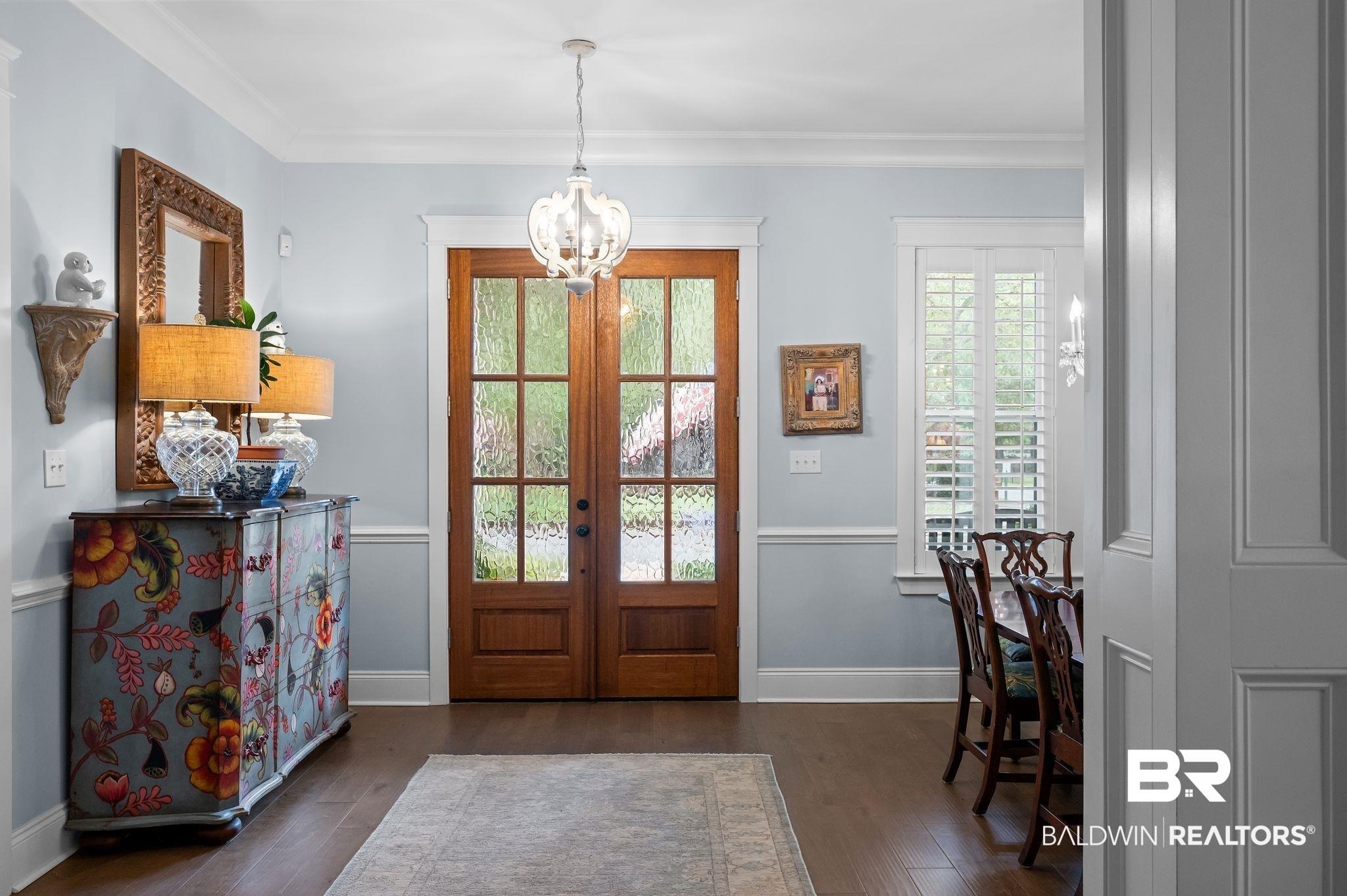 Image 4: Entryway featuring wood-finish flooring, a double-door entry with divided lites, a decorative chandelier, and crown molding