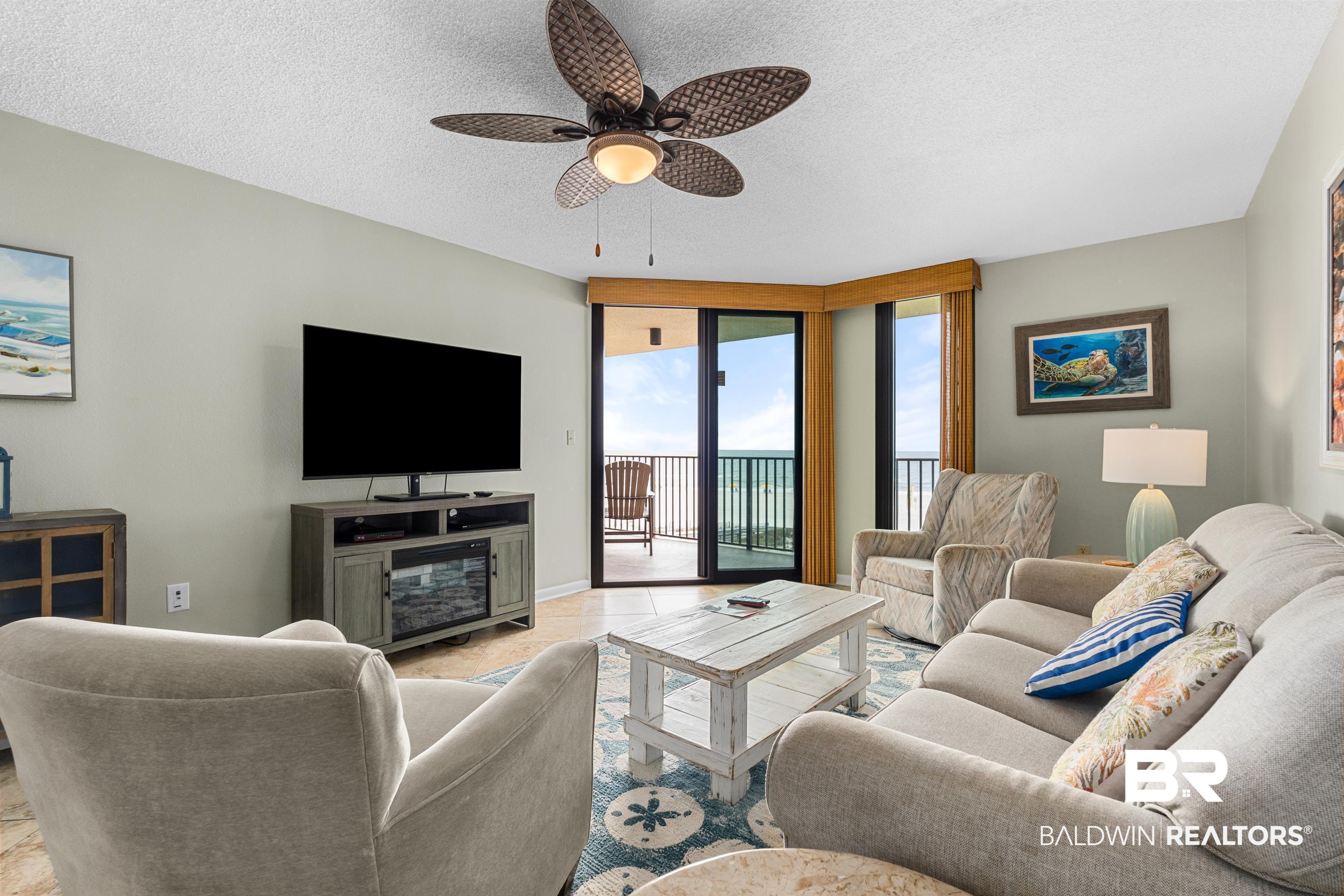 Image 3: Living area featuring a ceiling fan, wall-mounted television, and a balcony with waterfront scenery