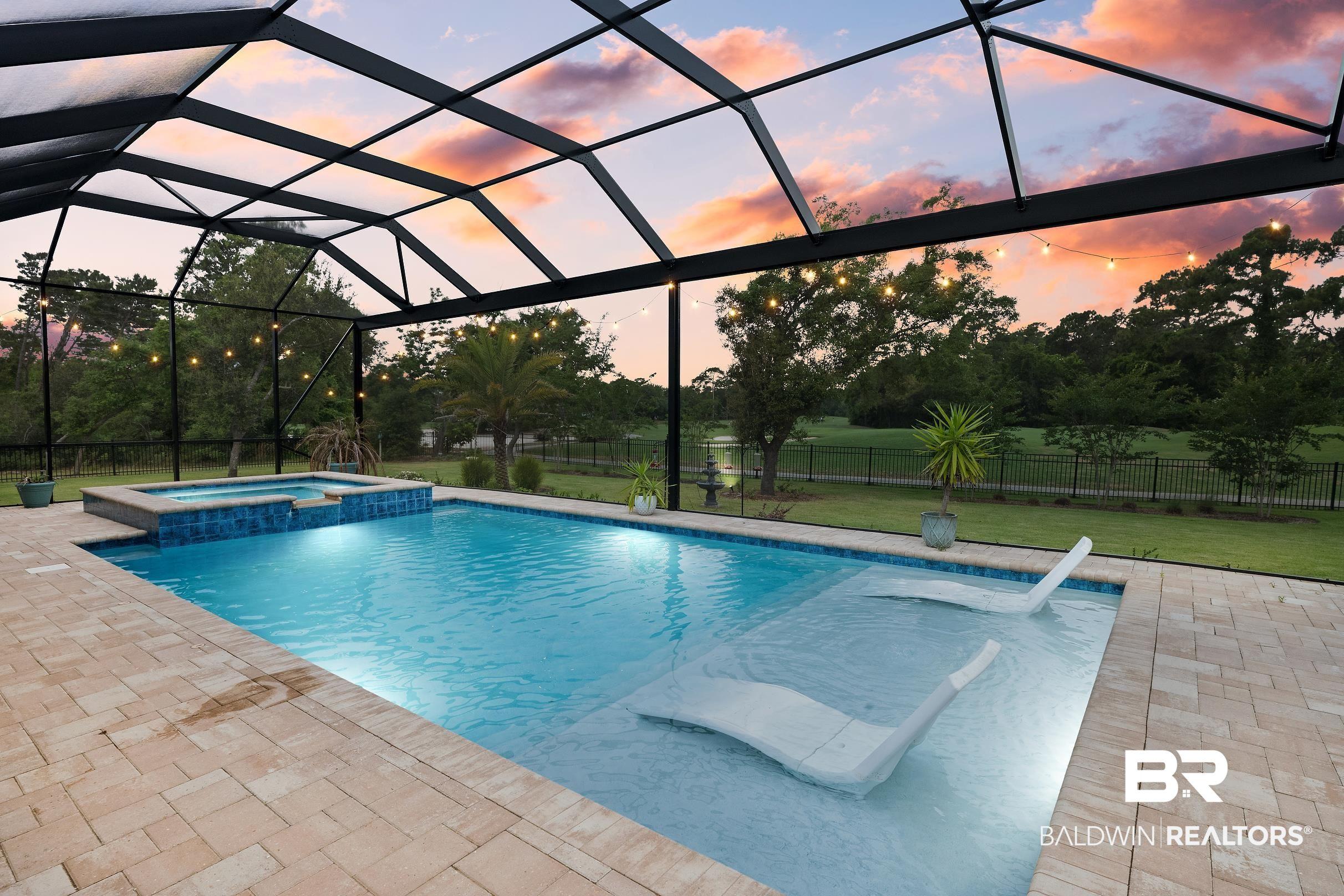 Image 2: Screen-enclosed pool area featuring a rectangular pool with integrated spa, paver decking, and string lighting