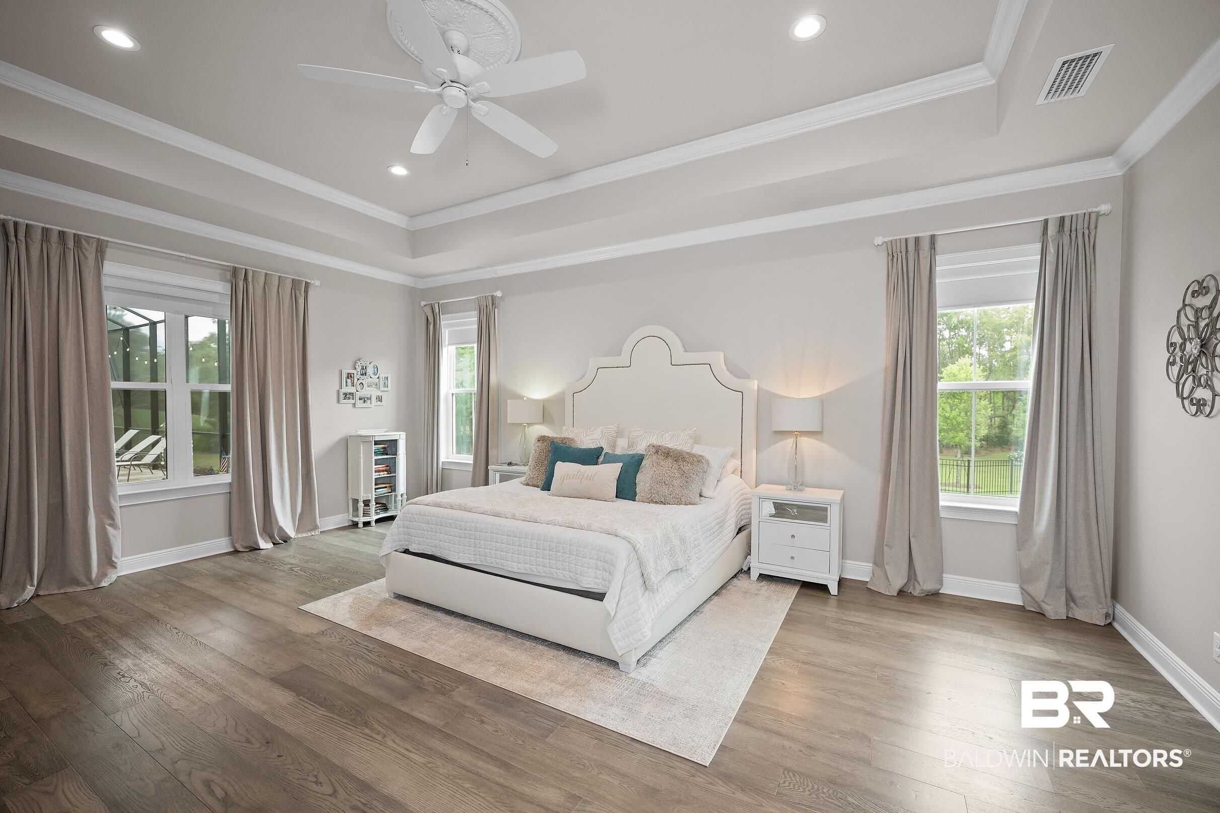 Image 4: Spacious room featuring wood-finish flooring, a tray ceiling with recessed lighting and a ceiling fan, and multiple windows with white trim