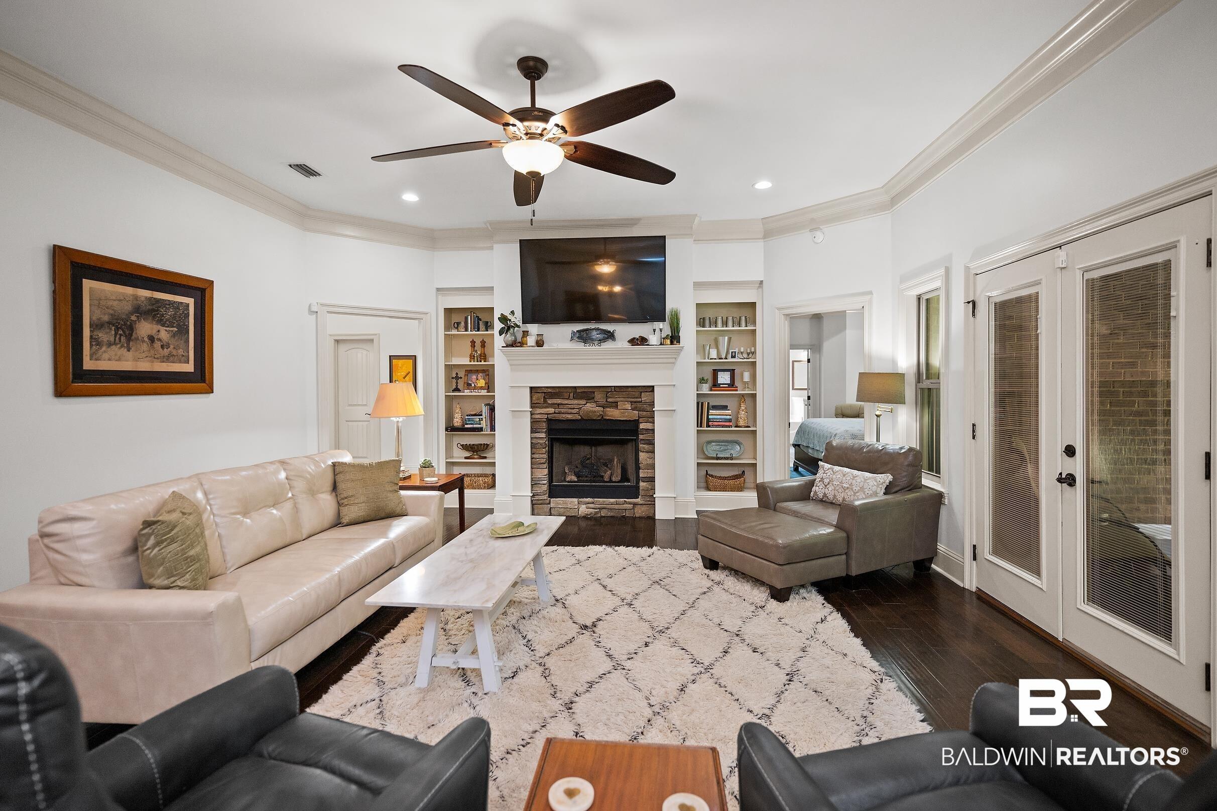 Image 4: Bright living area featuring dark wood-finish flooring, a stone-faced fireplace with a white mantel, and built-in shelving