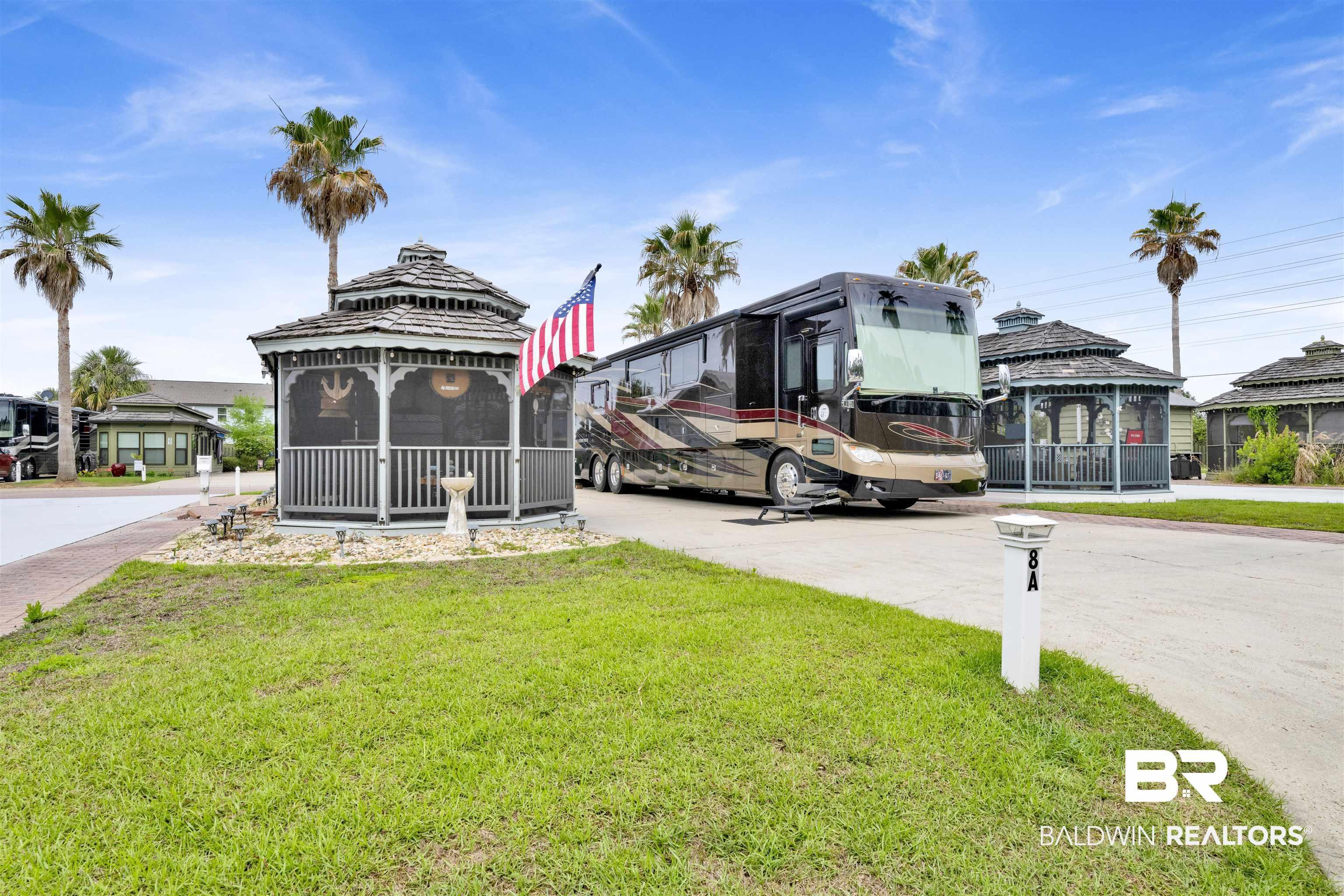 Image 1: Paved RV pad featuring a screened gazebo with a shingled roof, a manicured grass area, and mature palm trees