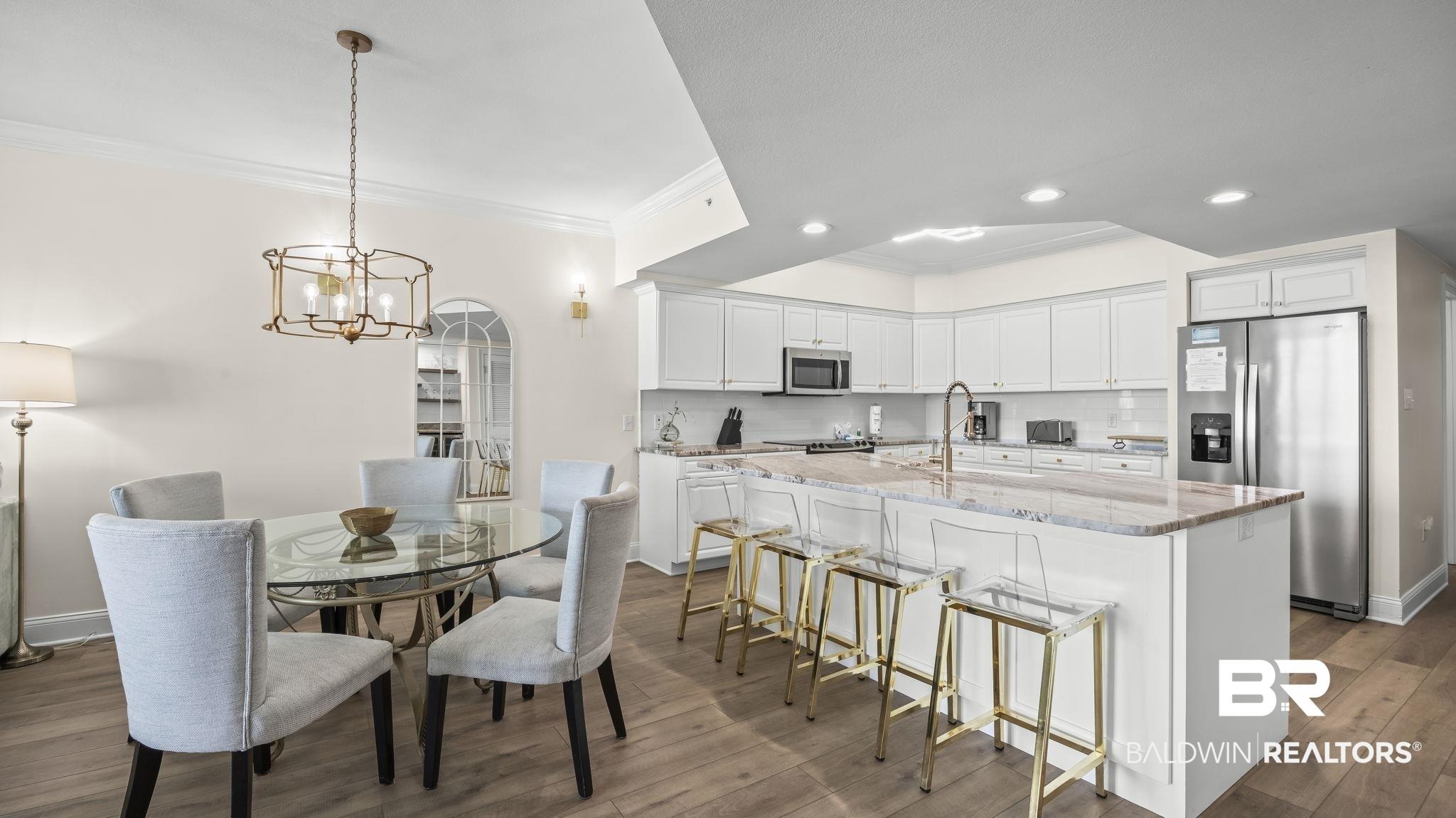 Image 4: Kitchen featuring stainless steel appliances, white cabinets, light stone counters, crown molding, and a center island with sink
