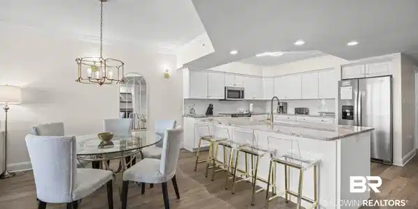 Image 4: Kitchen featuring stainless steel appliances, white cabinets, light stone counters, crown molding, and a center island with sink