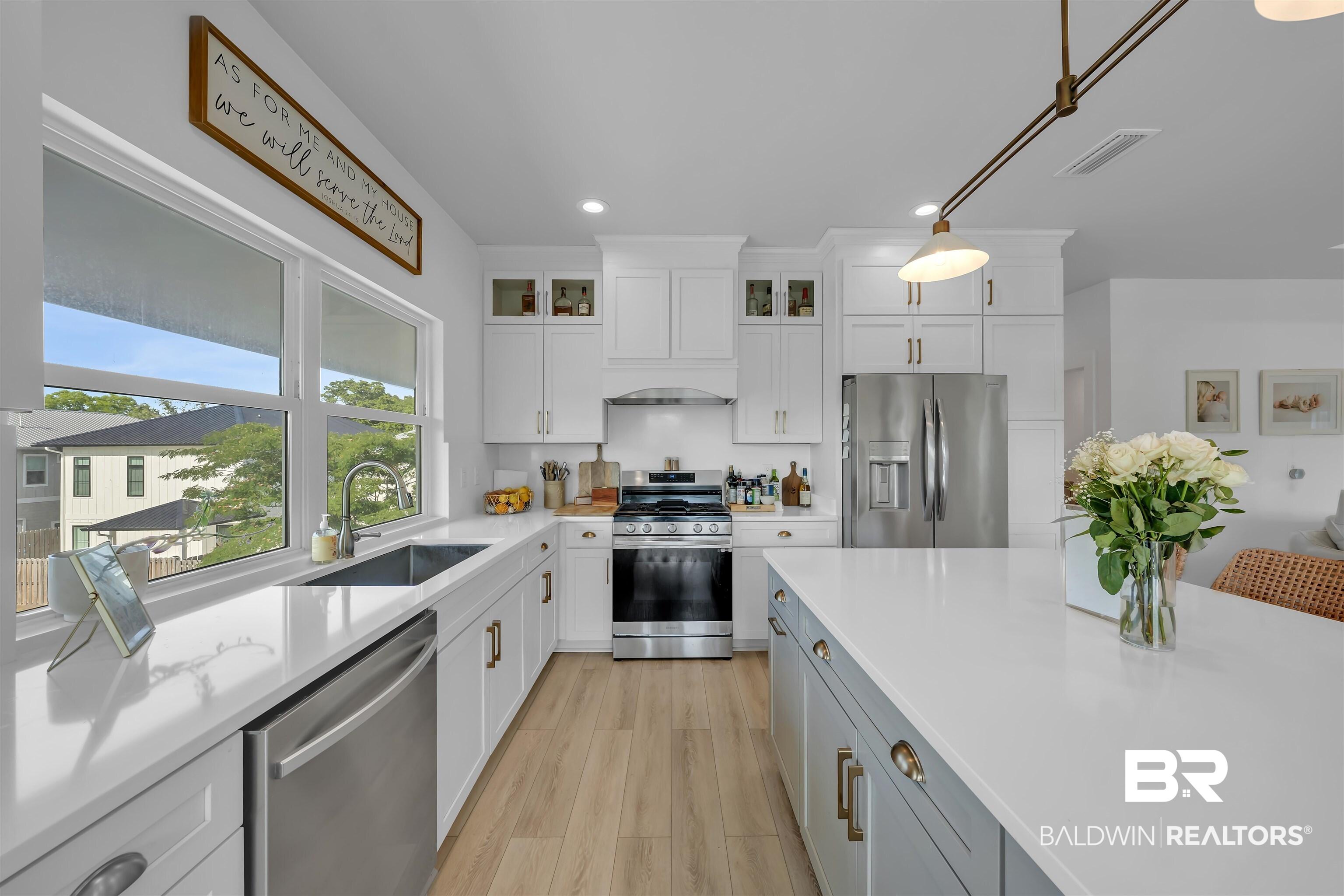 Image 3: Open-concept kitchen featuring white shaker cabinetry, stainless steel appliances, expansive white countertops, a large center island, and wood-finish flooring
