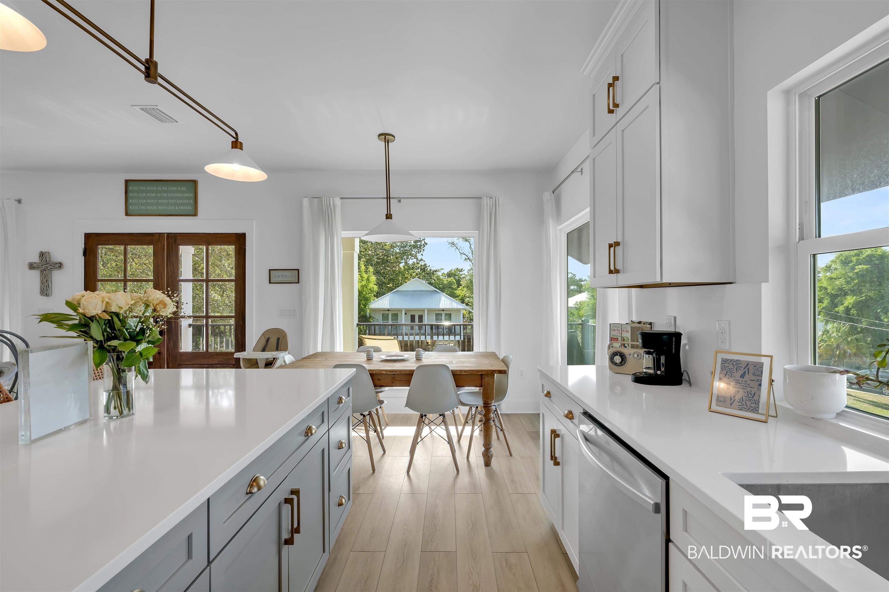 Image 4: Open-concept kitchen featuring white shaker cabinetry, an expansive island with gray base cabinets, wood-finish flooring, and bright windows