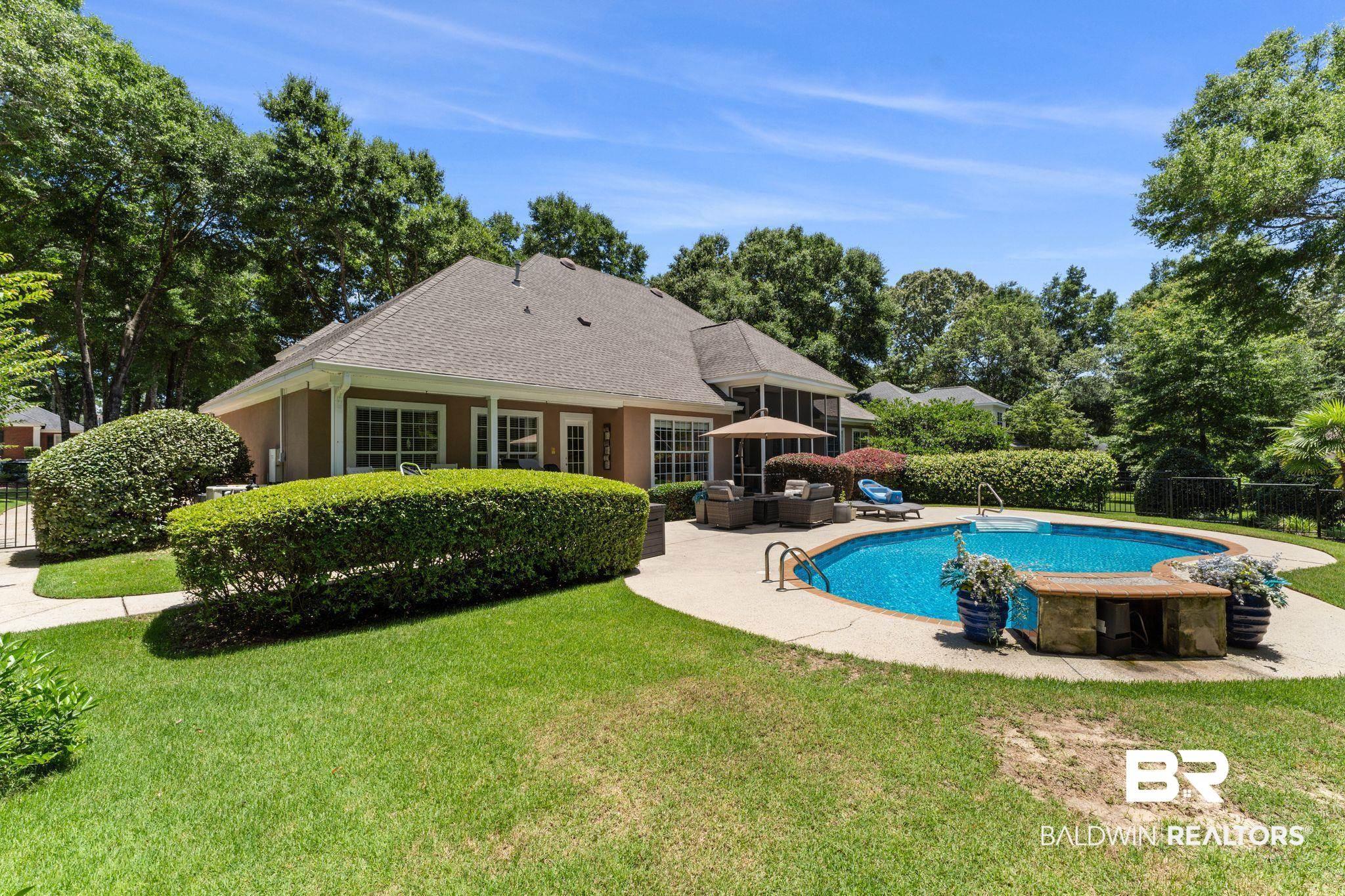 Image 2: Inviting backyard featuring a freeform swimming pool, concrete patio, screened-in porch, mature landscaping, and a stucco exterior
