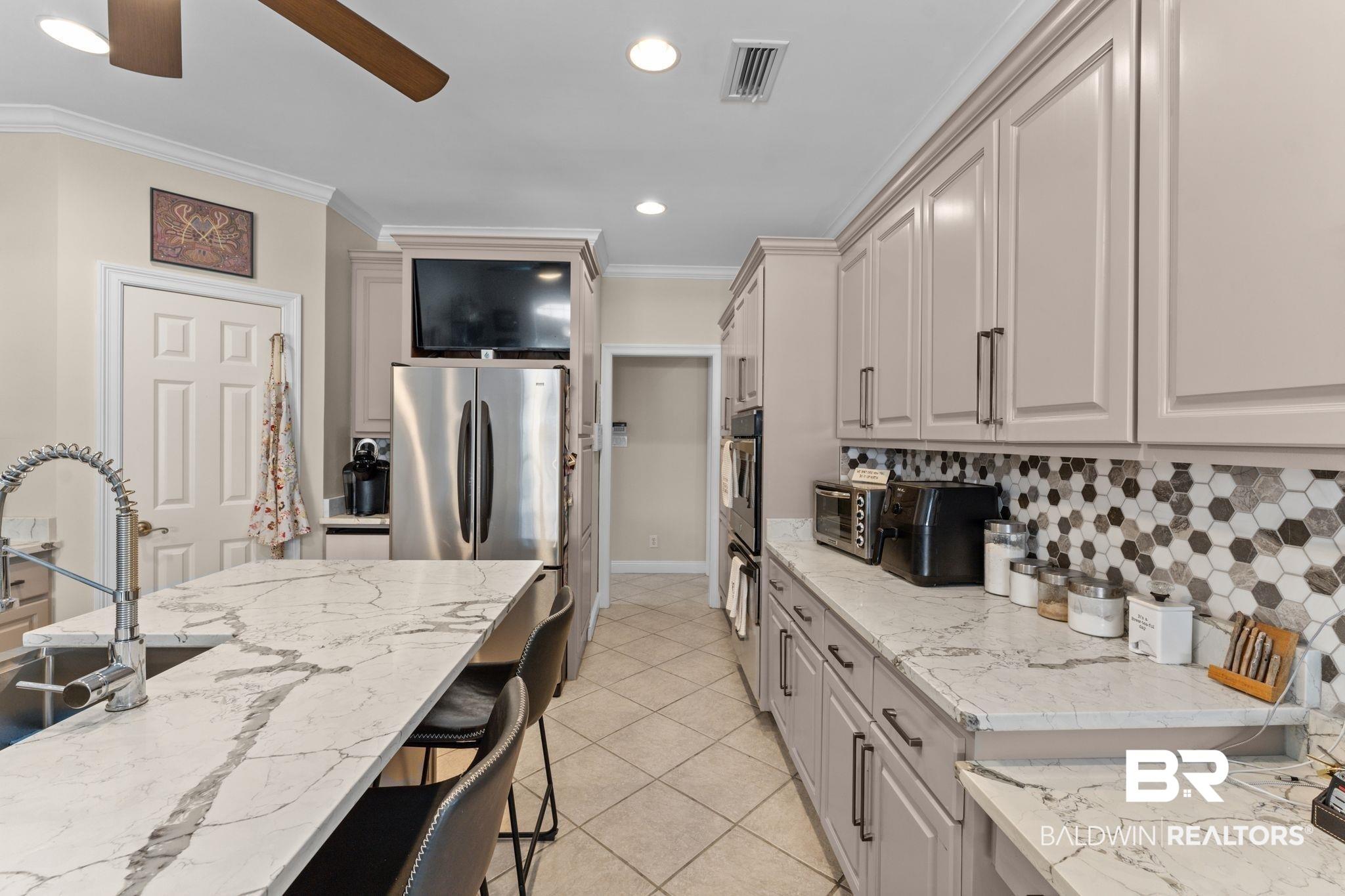 Image 4: Kitchen featuring an oversized island with an integrated sink, light-colored cabinetry with dark hardware, a hexagonal tile backsplash, light-toned countertops, and recessed lighting