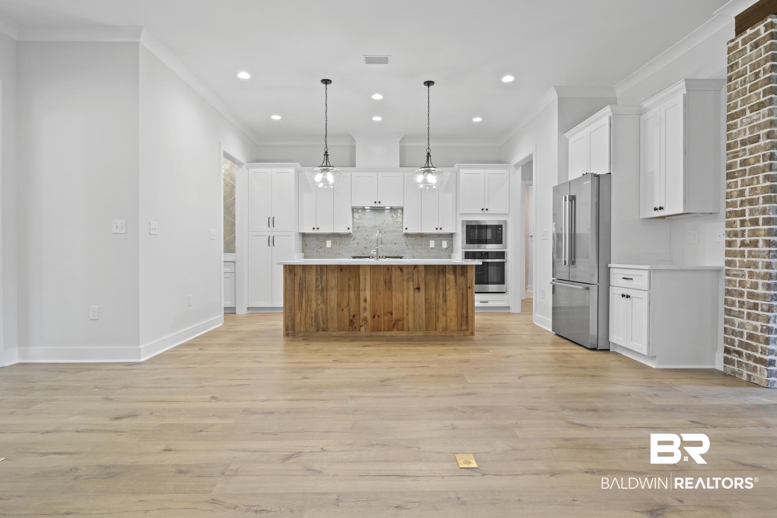 Image 4: Kitchen featuring white cabinetry, light hardwood / wood-style flooring, stainless steel fridge, an island with sink, and pendant lighting