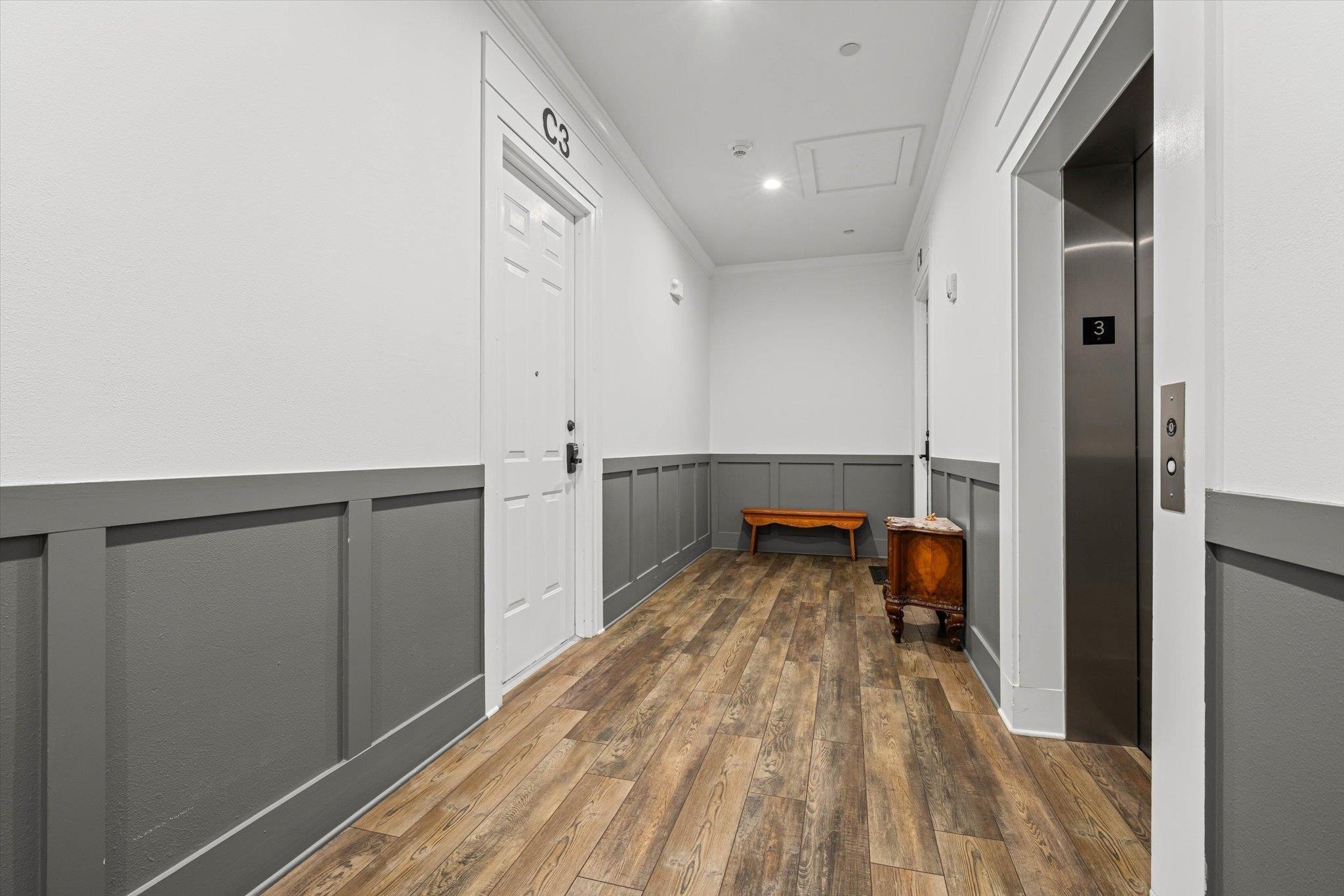 Image 2: Hall with wainscoting, ornamental molding, a decorative wall, attic access, and dark wood finished floors