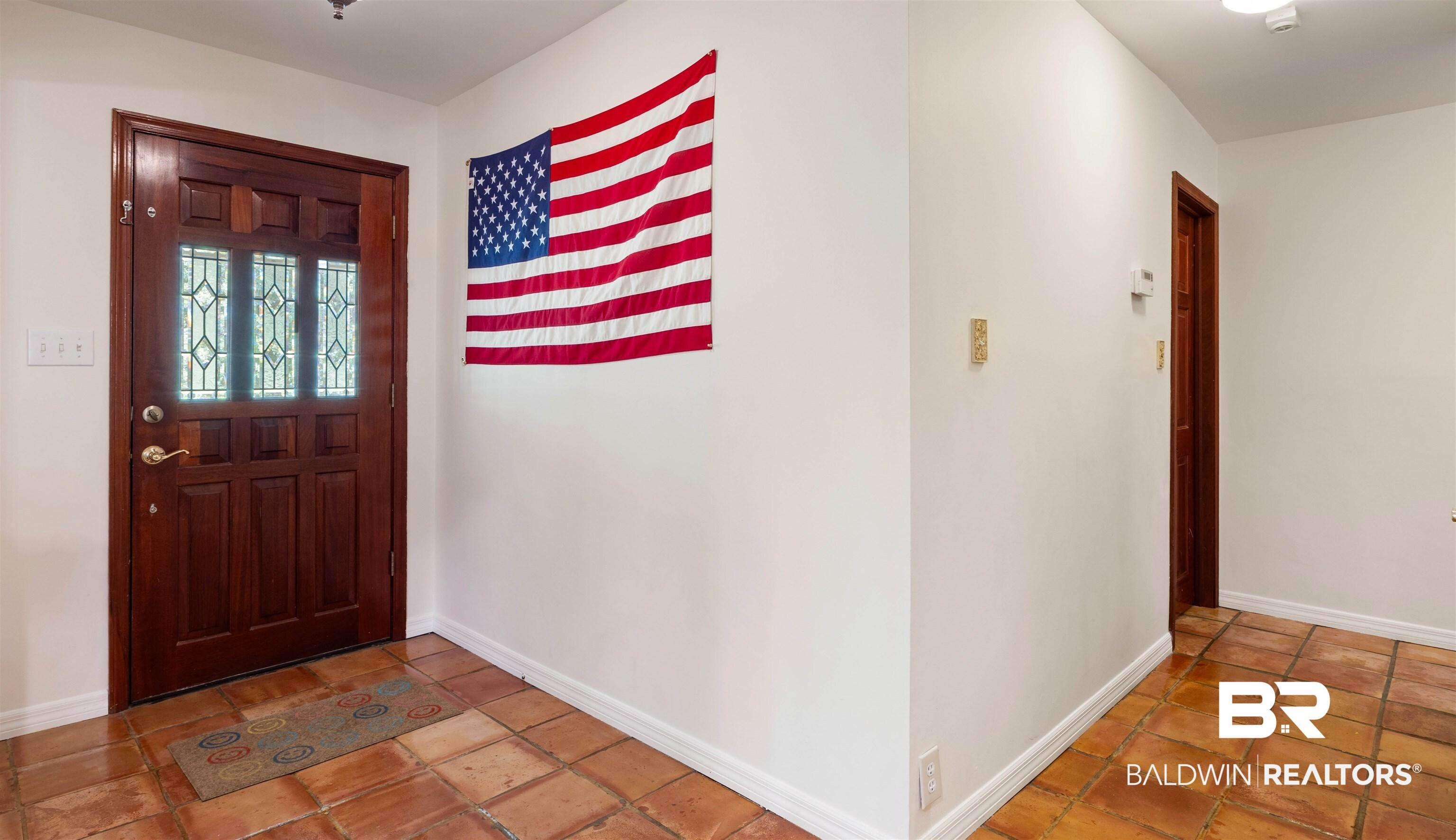 Image 2: Entryway featuring a paneled wood-finish door with decorative glass inserts, terracotta-style floor tiles, white baseboards, and neutral wall tones