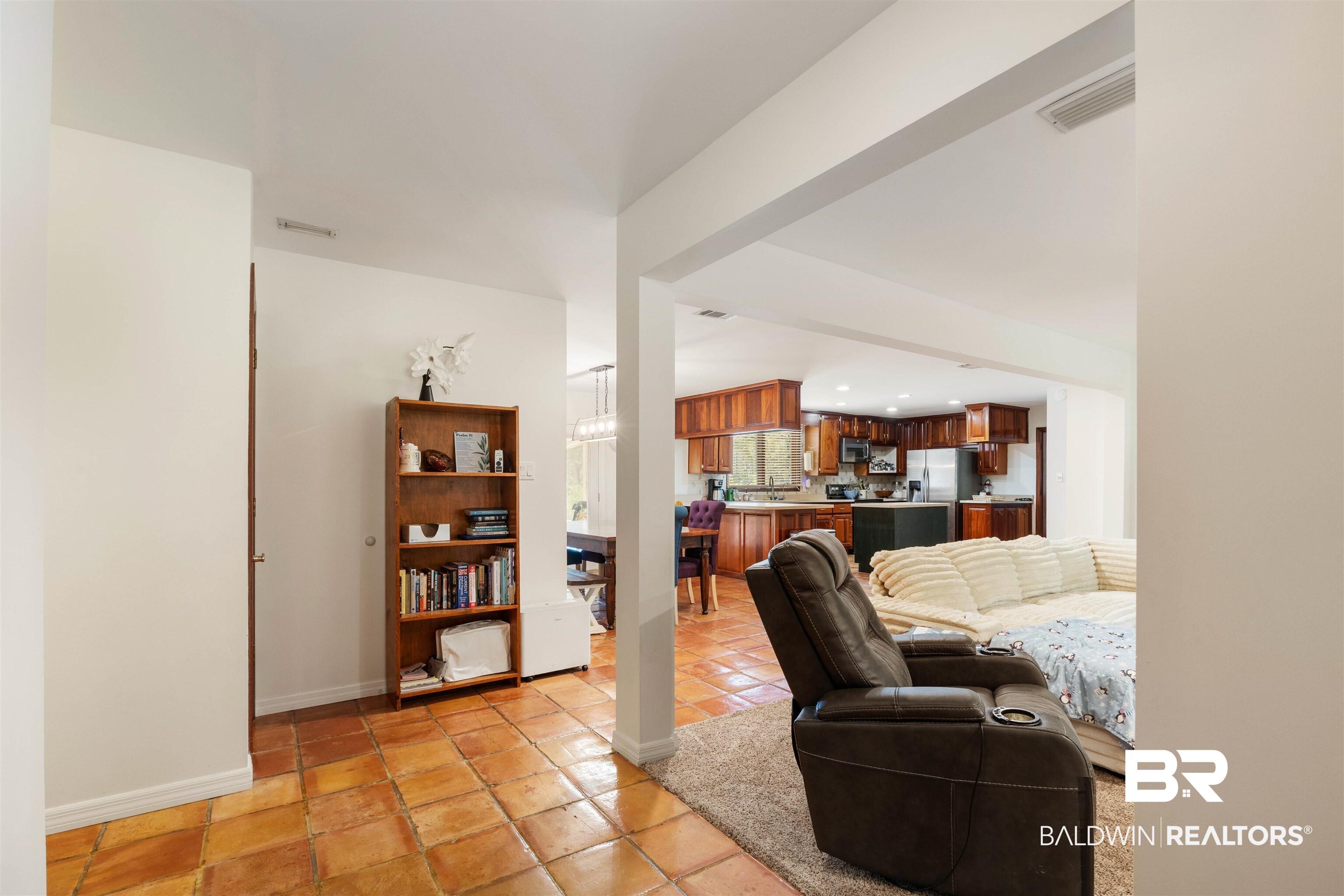 Image 3: Open-concept living space featuring terracotta-style floor tiling, a kitchen with wood cabinetry and stainless steel appliances, and a dining area