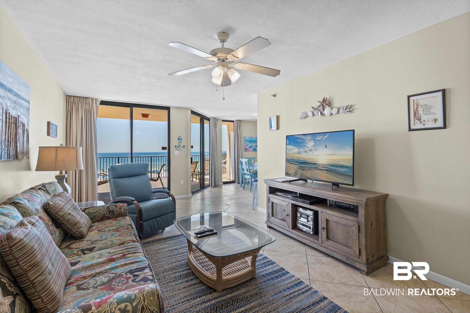 Image 2: Living area featuring tiled flooring, a ceiling fan with integrated lighting, and direct access to a balcony with ocean views through sliding glass doors