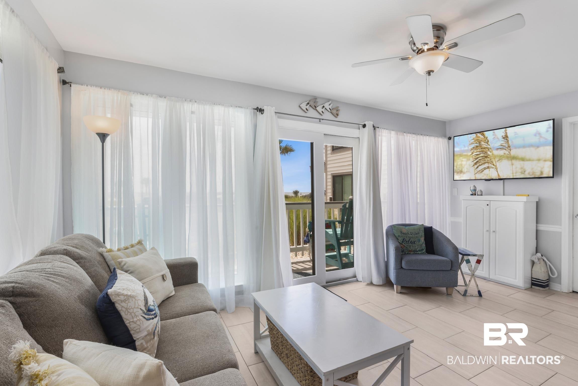 Image 2: Living area with light-toned wood-finish flooring, a ceiling fan with integrated lighting, and a sliding glass door opening to an outdoor deck