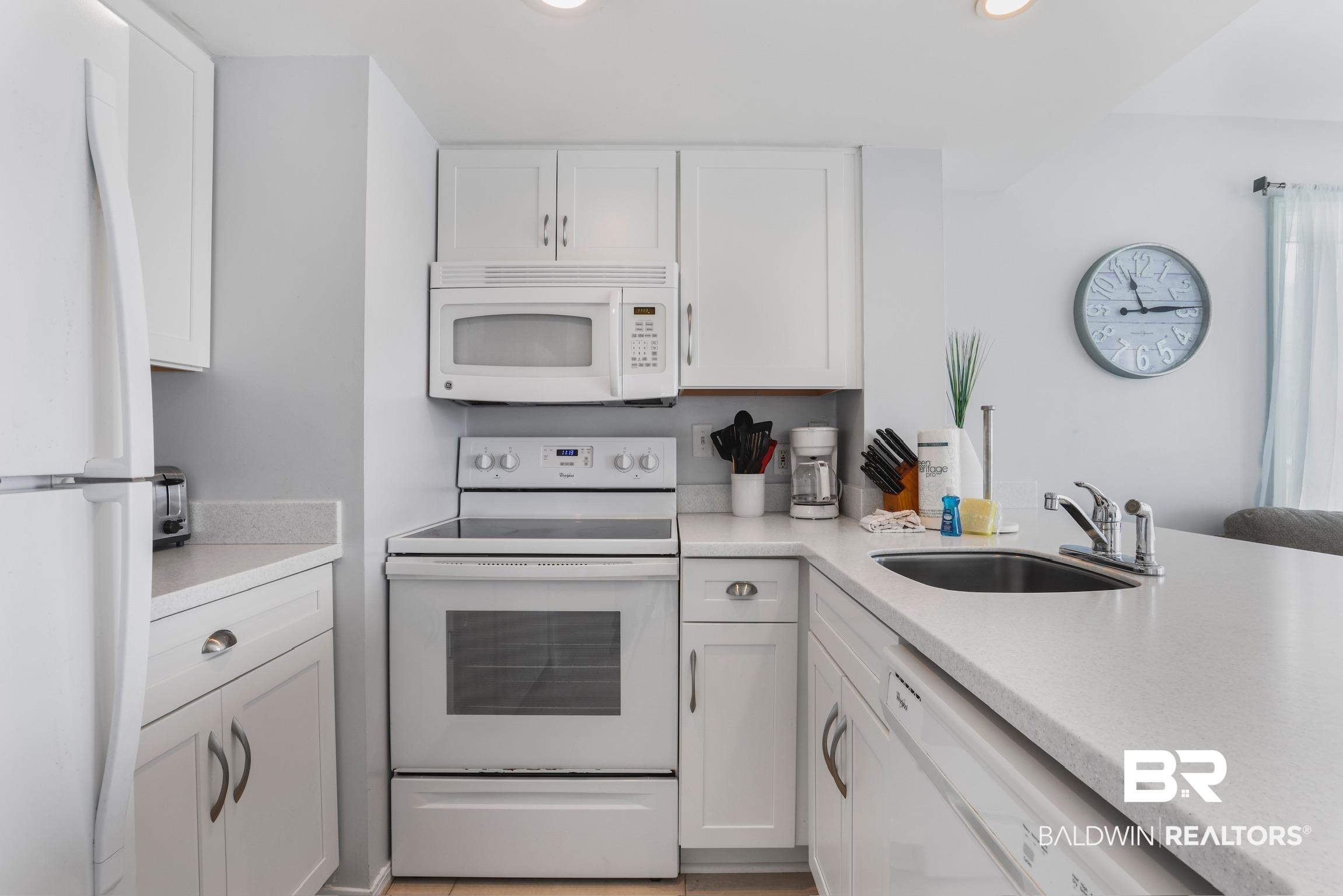 Image 3: Full kitchen featuring white cabinetry, light-toned countertops, white appliances, and a stainless steel sink with a chrome faucet