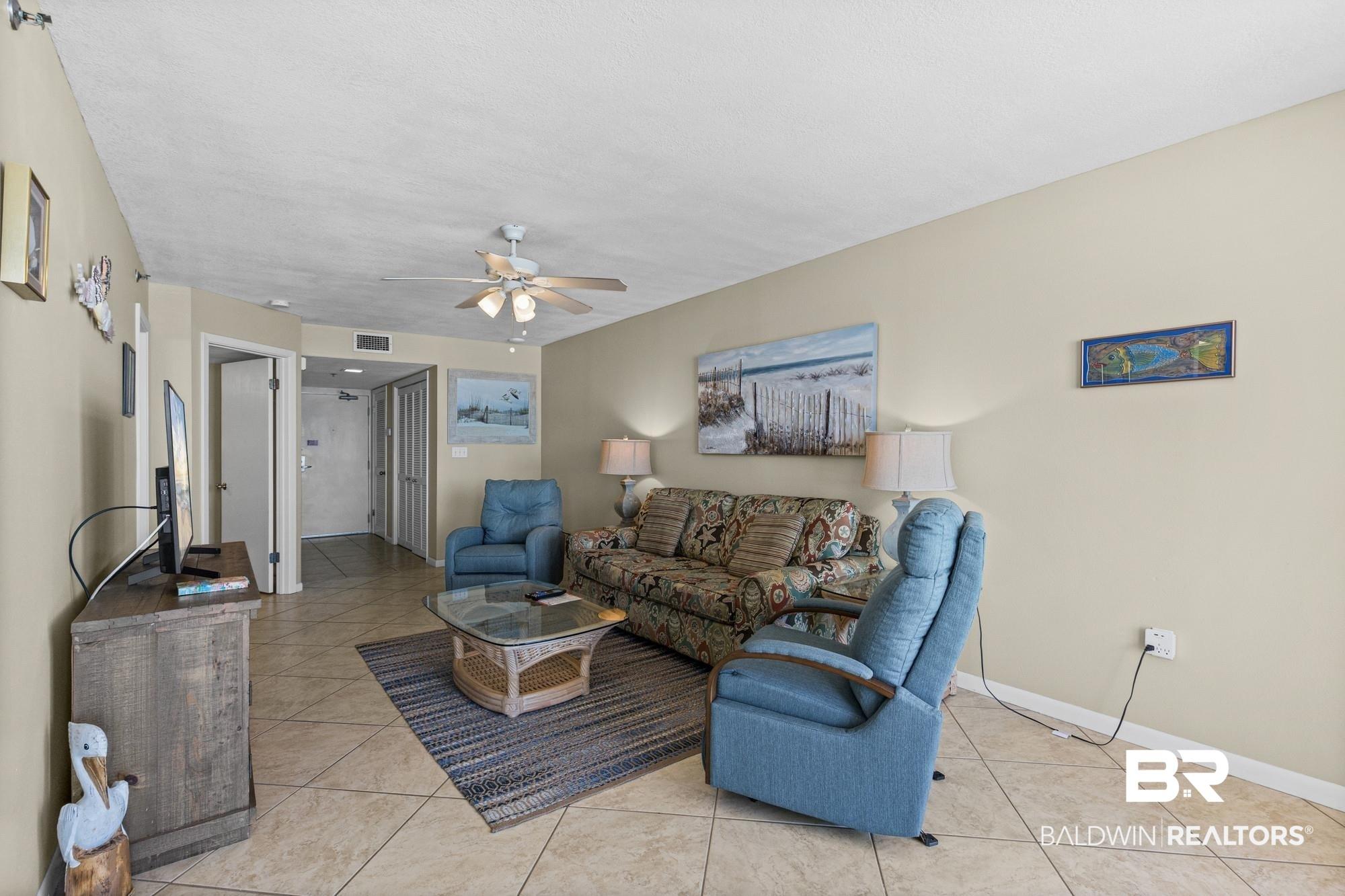 Image 4: Living area featuring neutral wall tones, tile flooring, and a ceiling fan with integrated lighting