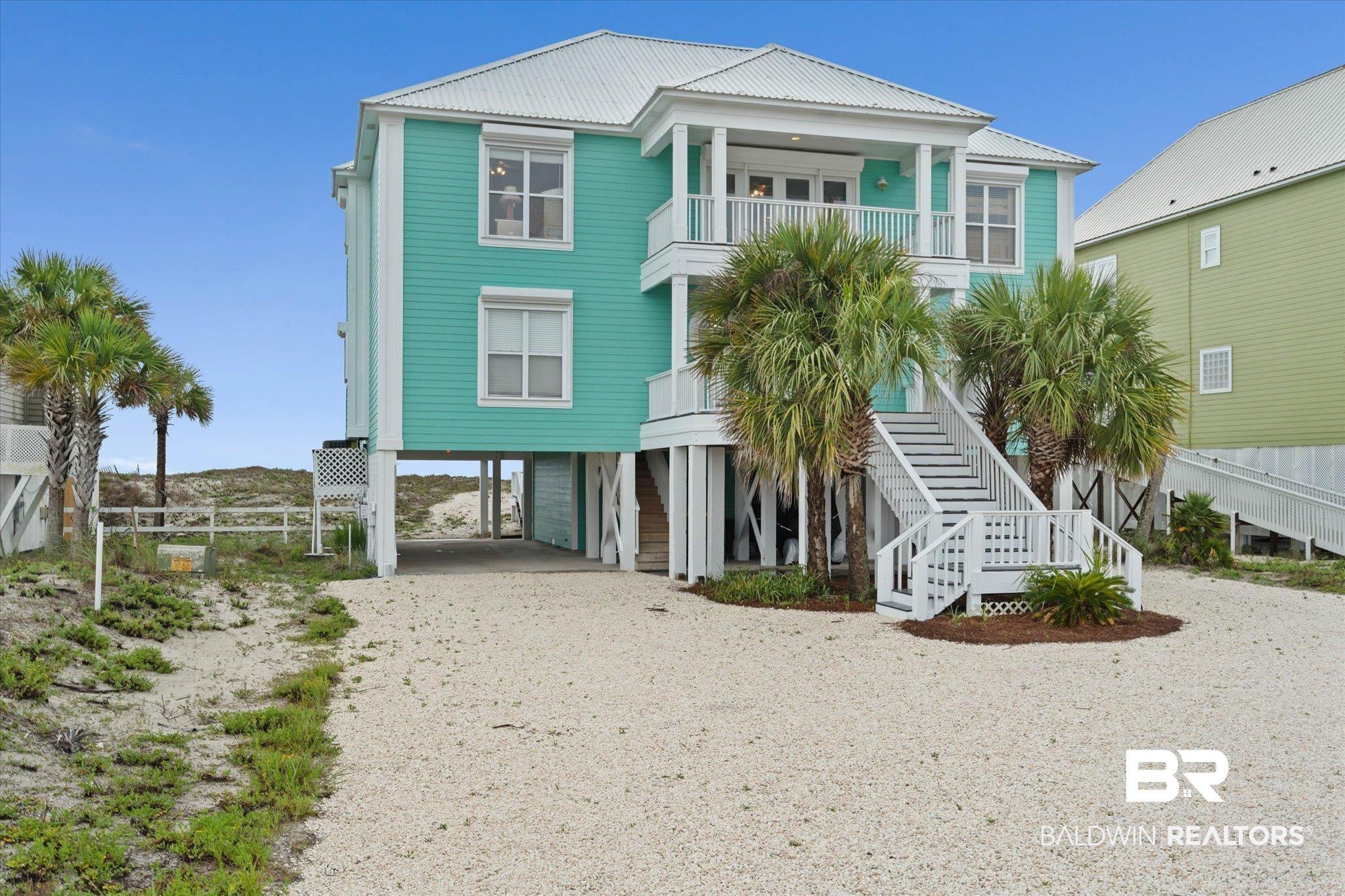 Image 2: Stilted coastal residence featuring a teal exterior, white metal roof, and a gravel driveway