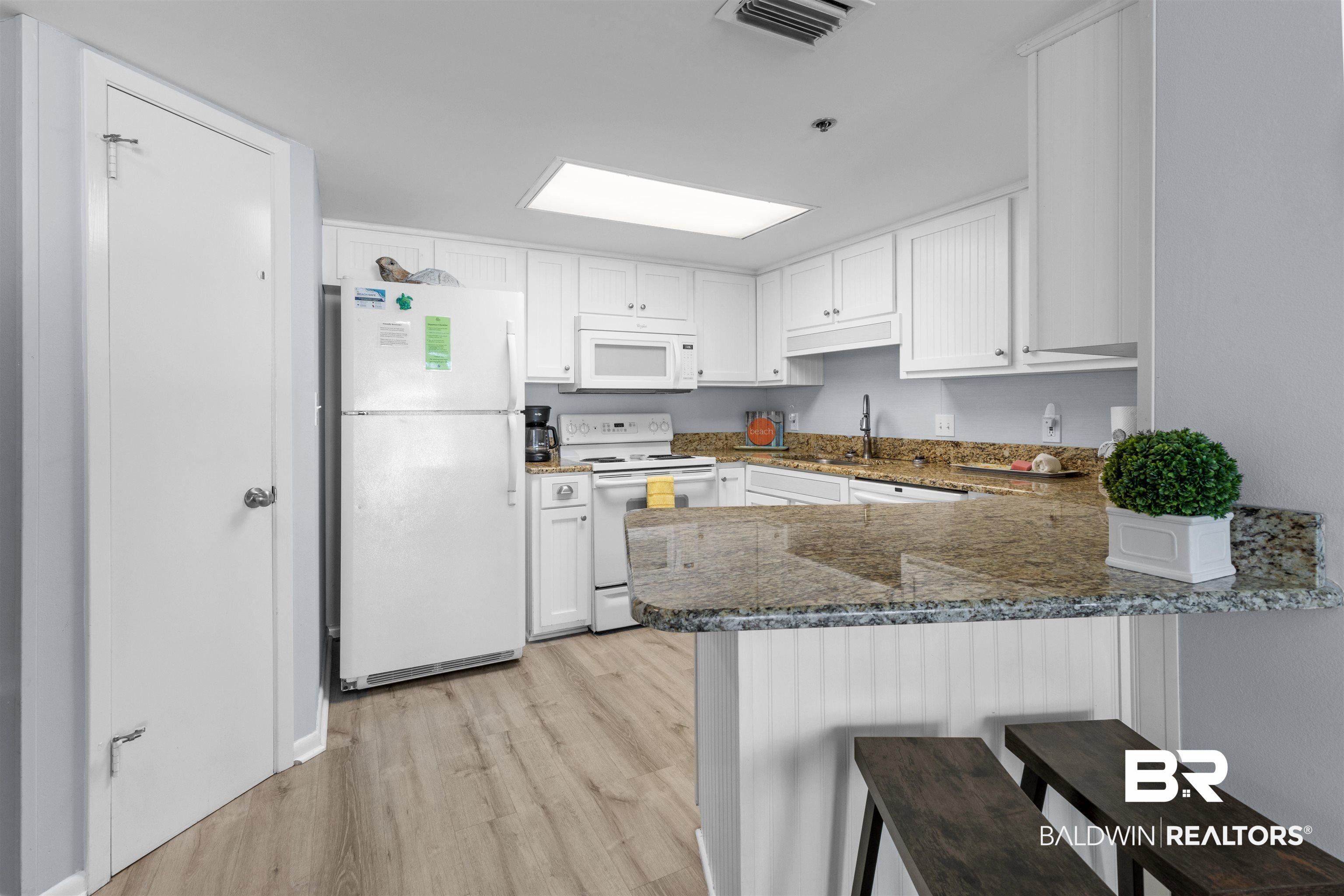 Image 3: Kitchen with white appliances, white cabinets, dark stone counters, and a breakfast bar area
