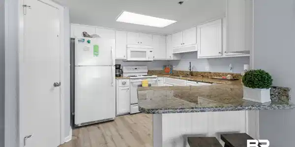 Image 3: Kitchen with white appliances, white cabinets, dark stone counters, and a breakfast bar area