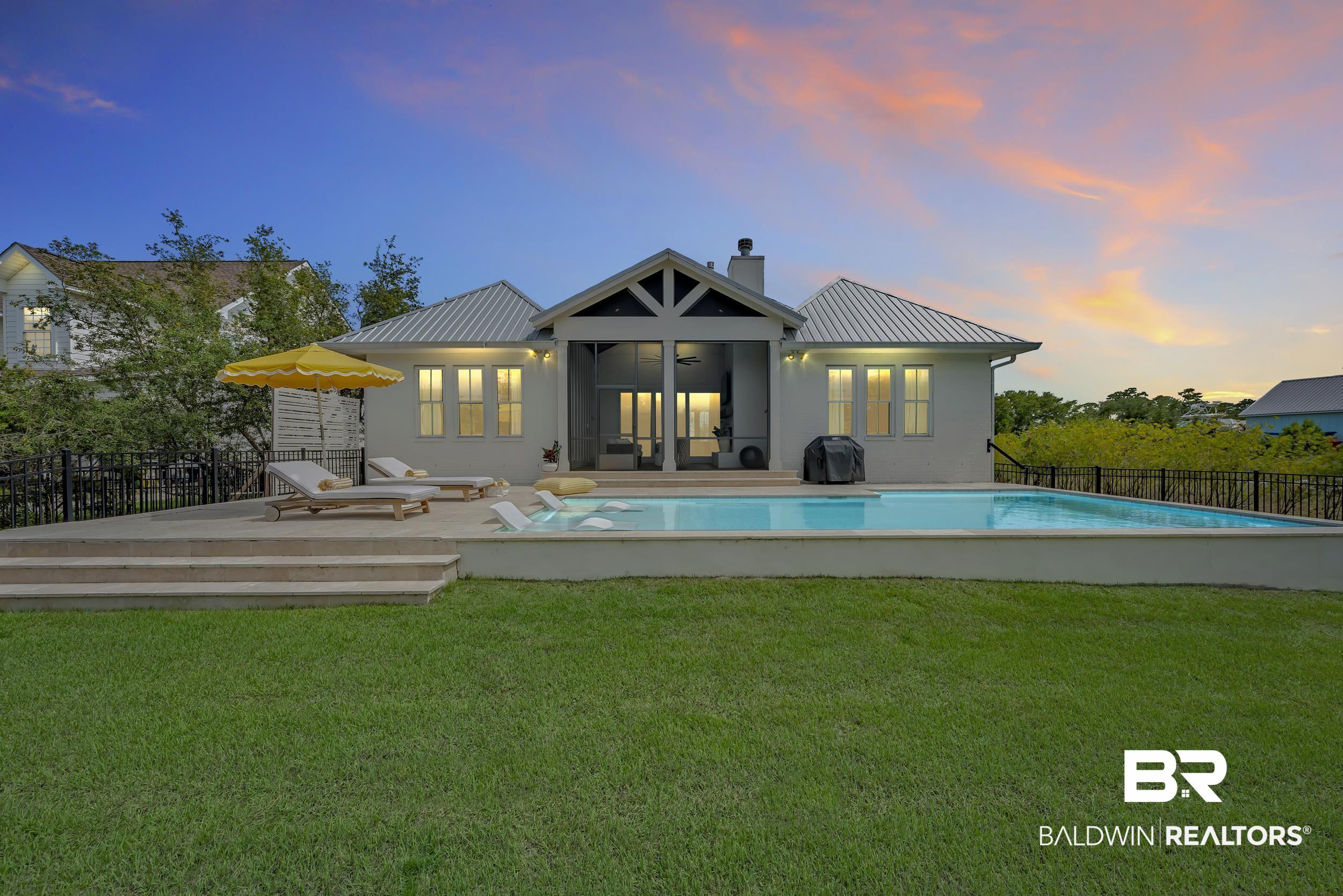 Image 3: Rear exterior featuring a rectangular pool with a surrounding concrete patio, a covered porch, and a metal roof