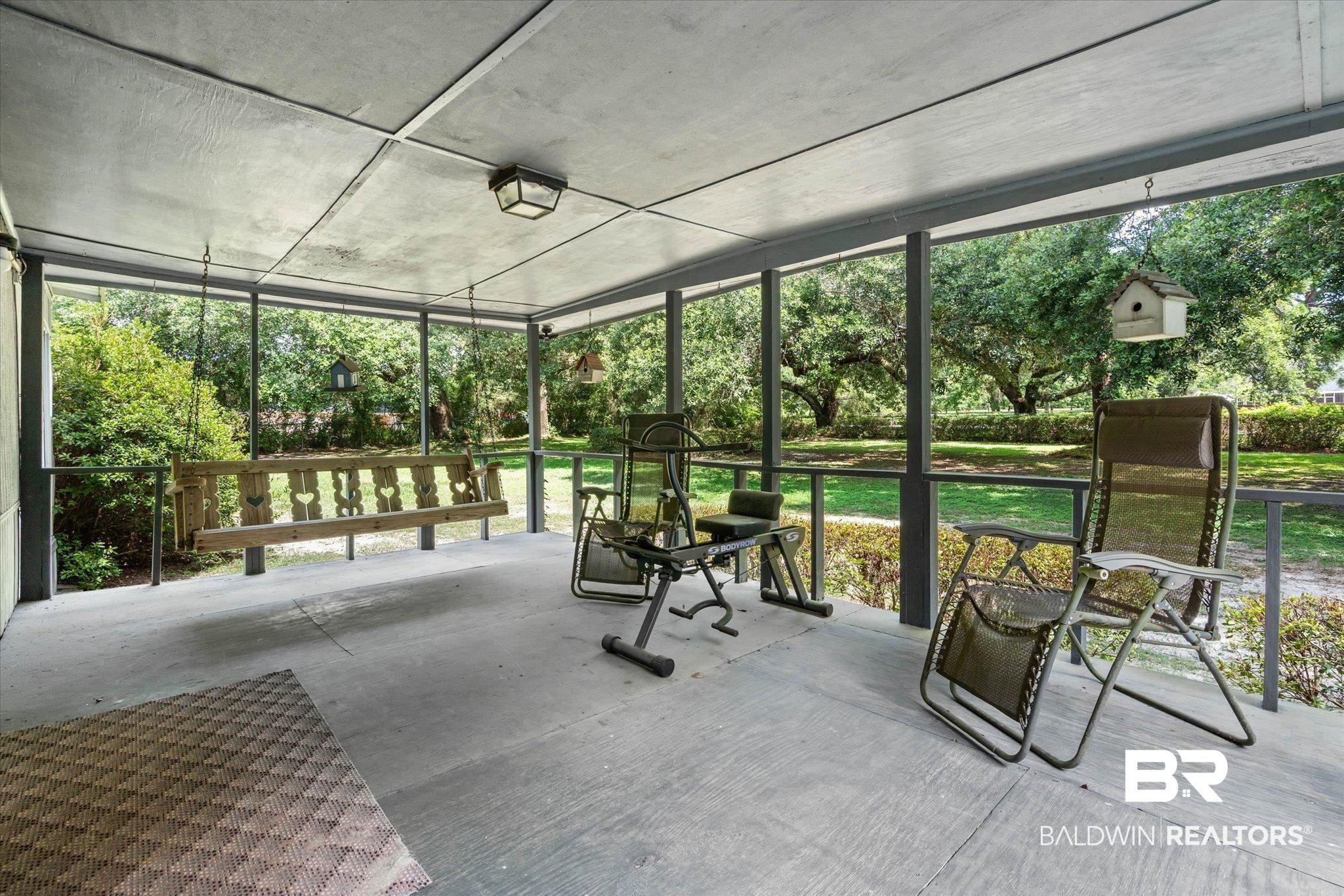 Image 2: Spacious screened porch featuring a concrete floor, overhead lighting fixture, and a wooden porch swing
